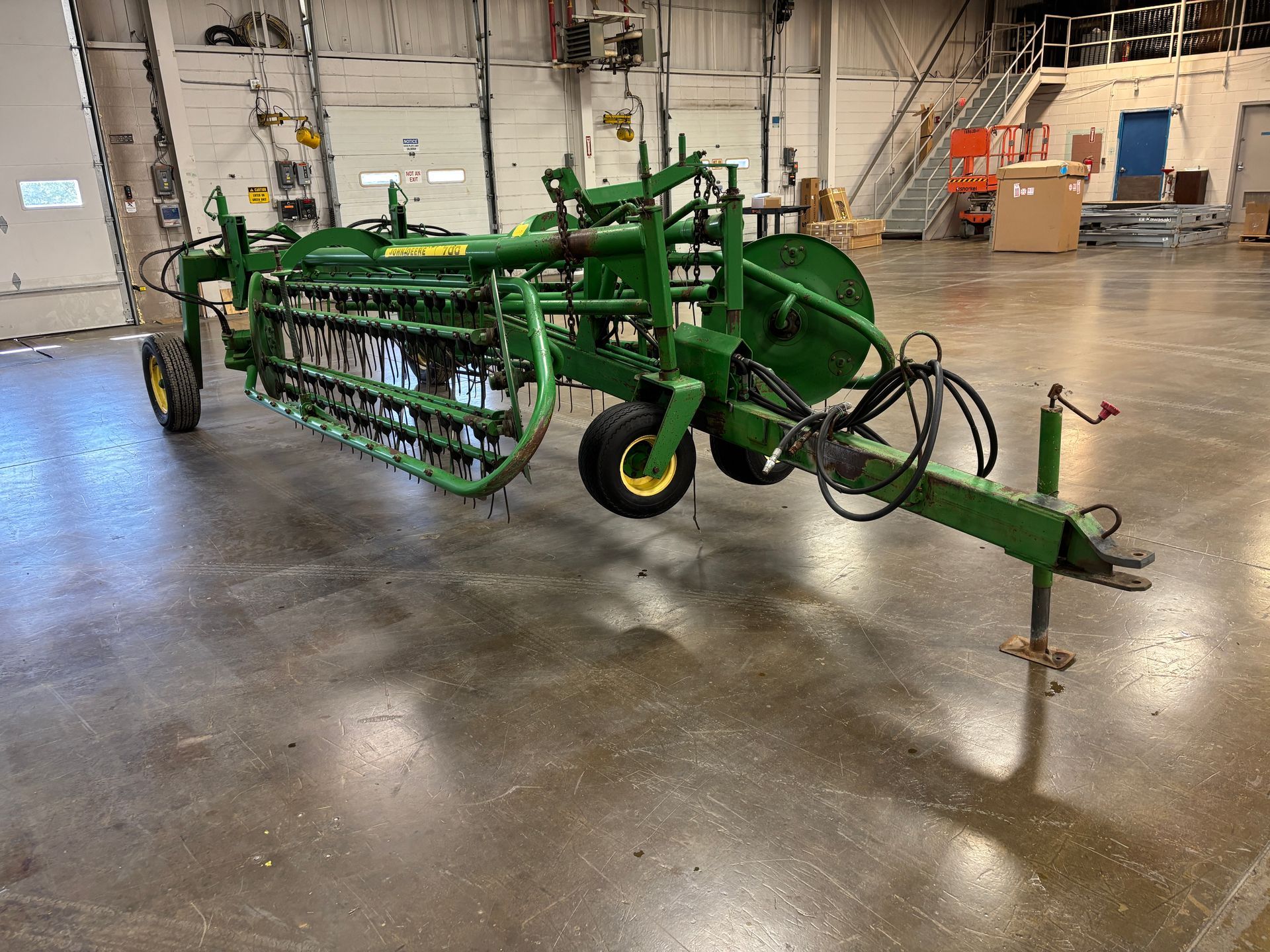 Green John Deere hay rake in a large indoor space.