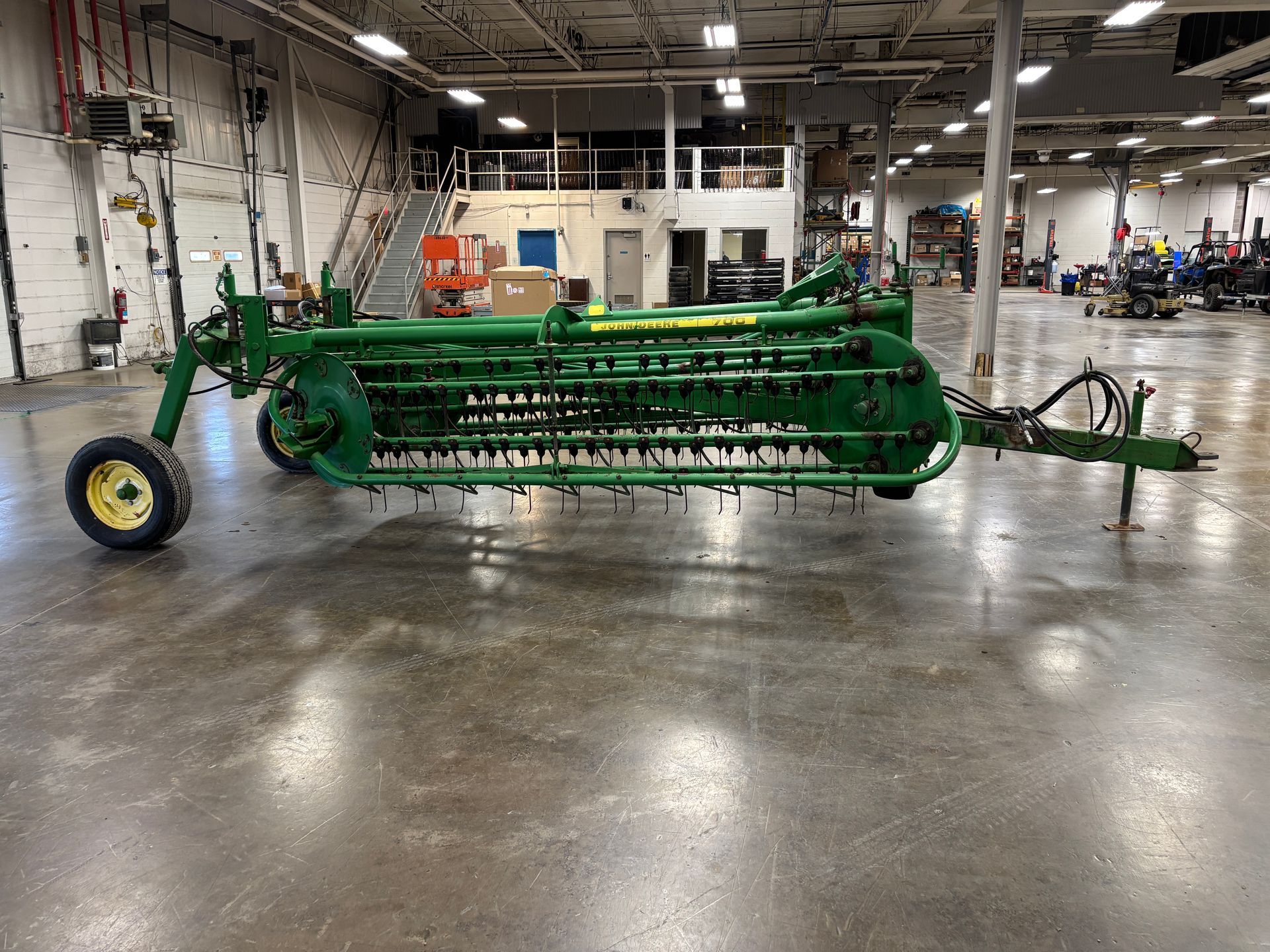 Green John Deere hay rake in an industrial setting.