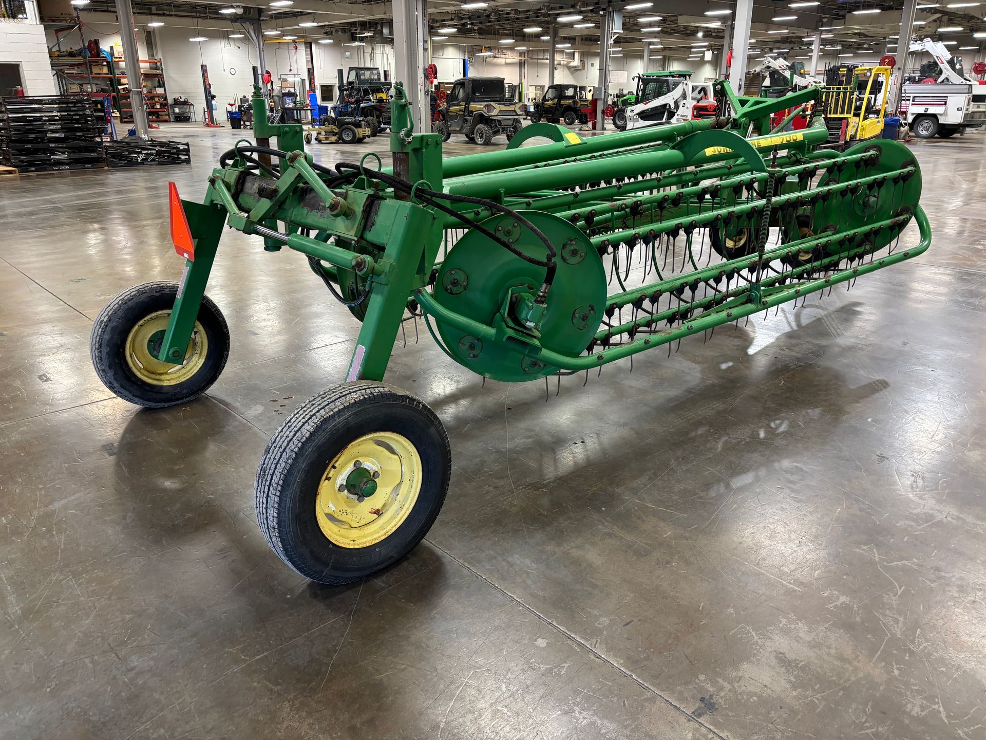 Green John Deere hay rake on a gray concrete floor.