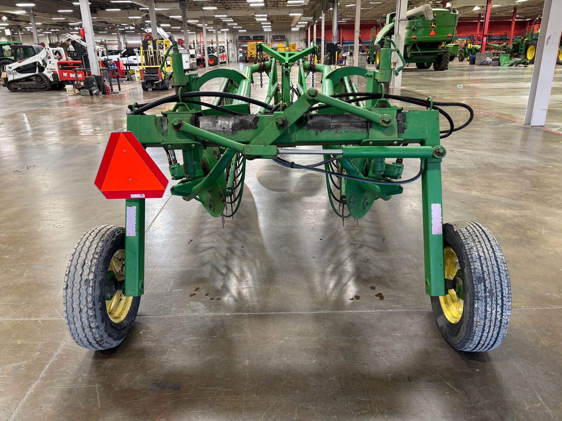 John Deere hay rake with green frame, two wheels, and an orange safety triangle.