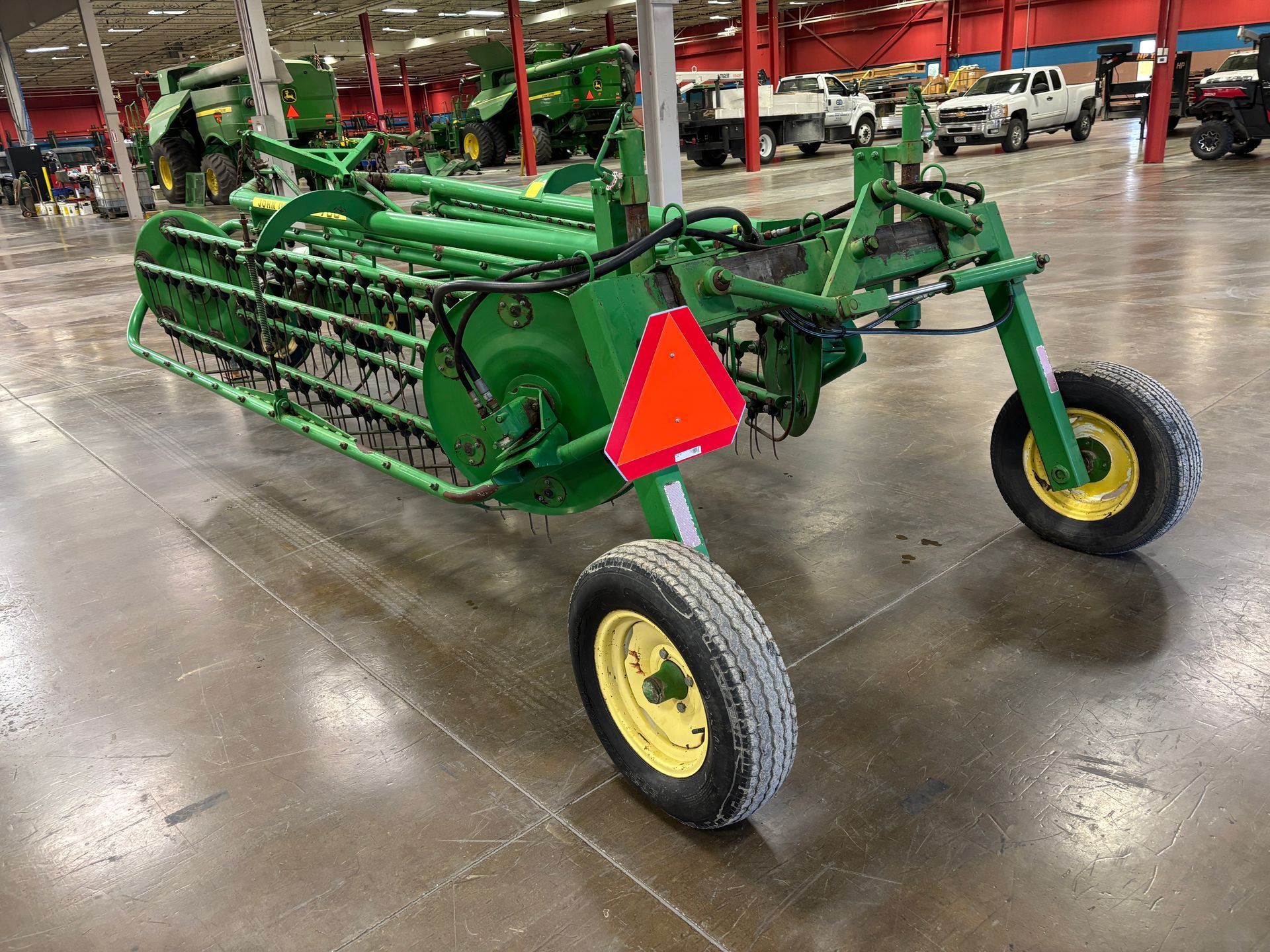 John Deere hay rake, green and yellow, in an indoor space with a red triangle sign.