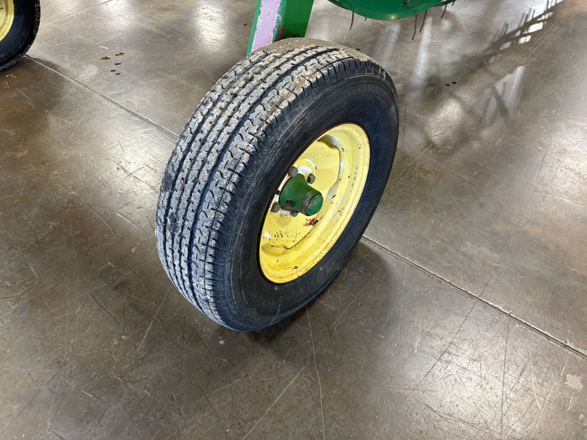 Black tire with worn tread on a yellow wheel. Green hubcap on a concrete floor.