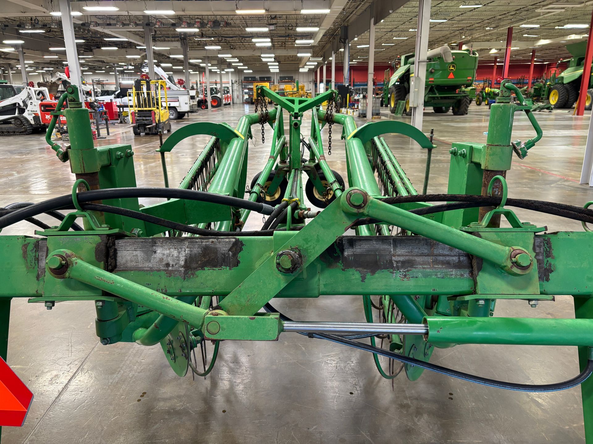 Green John Deere hay rake in a large warehouse.