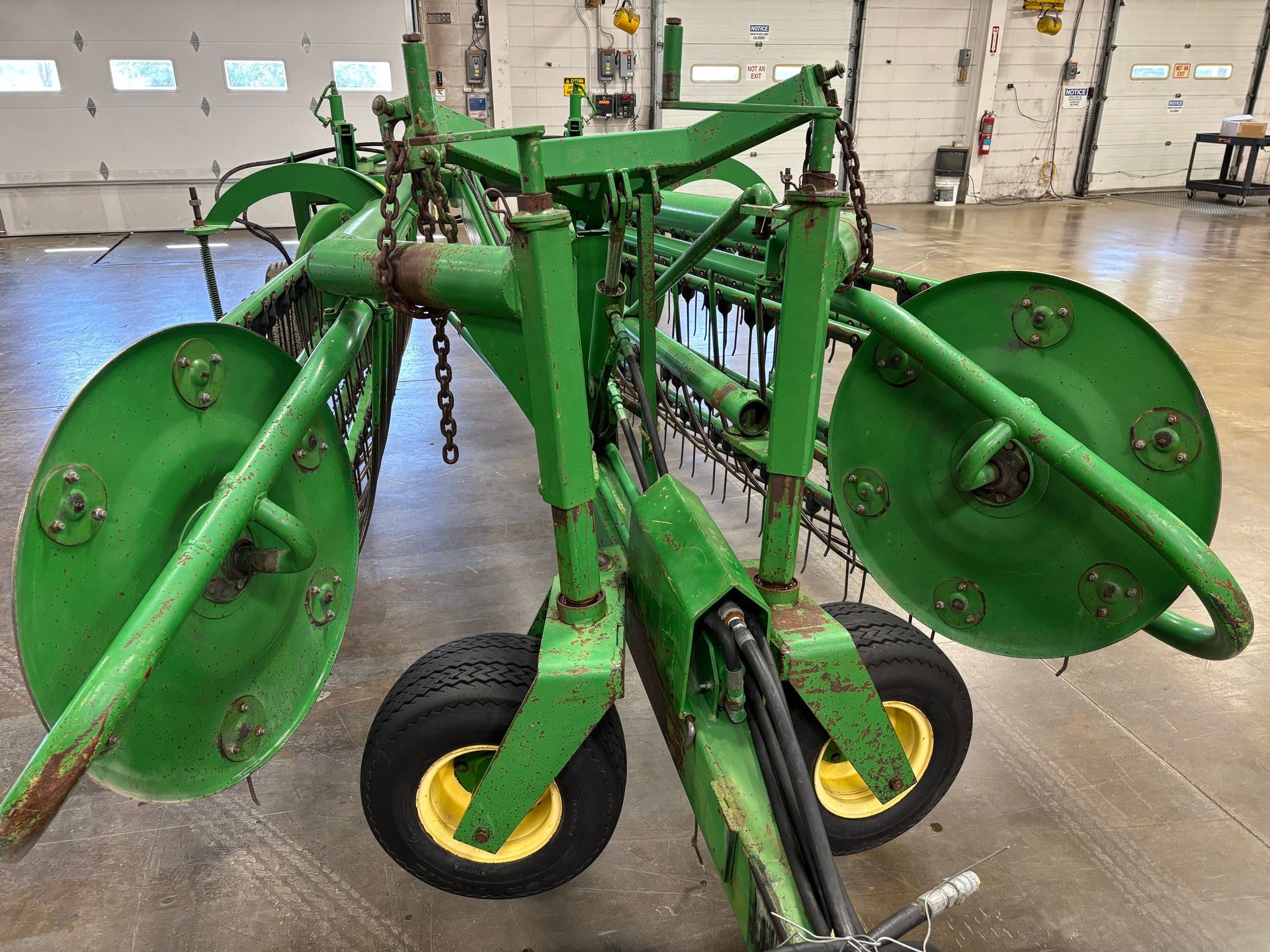 Green John Deere hay rake in a garage.