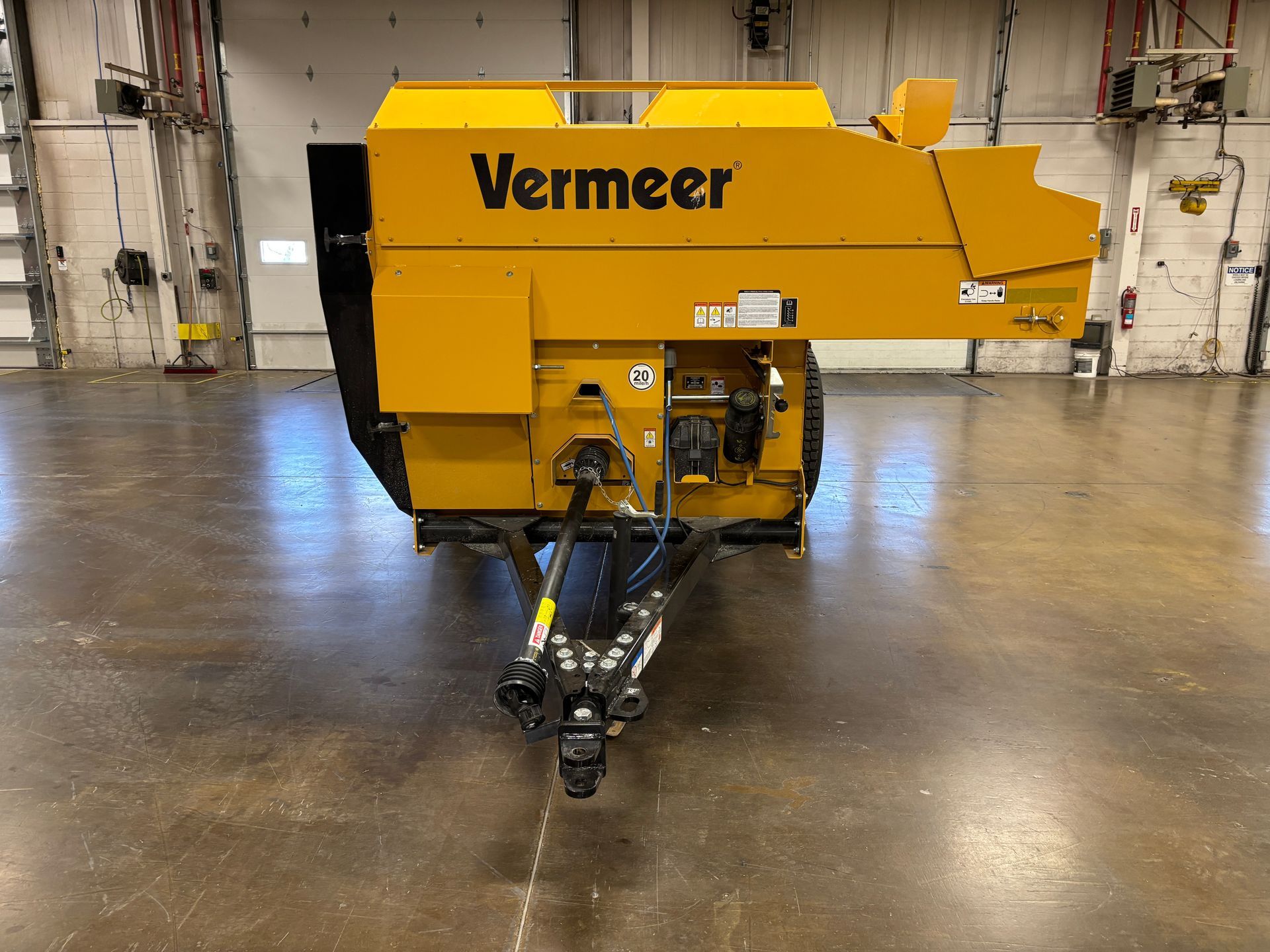 Yellow Vermeer hay baler on trailer, parked in a warehouse.