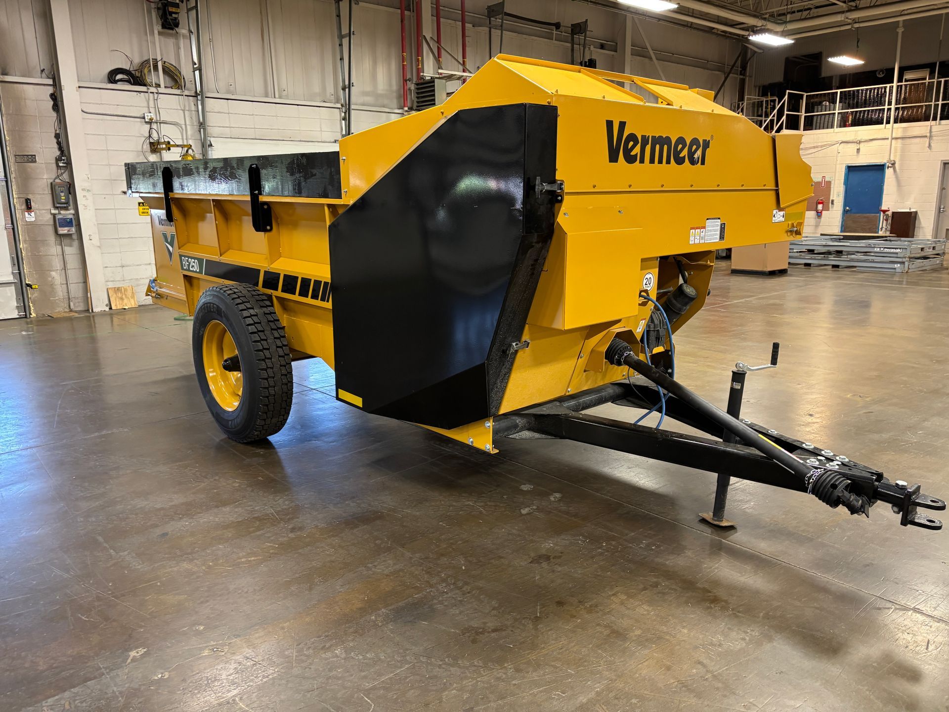 Yellow Vermeer manure spreader with black accents and a single wheel in an industrial setting.