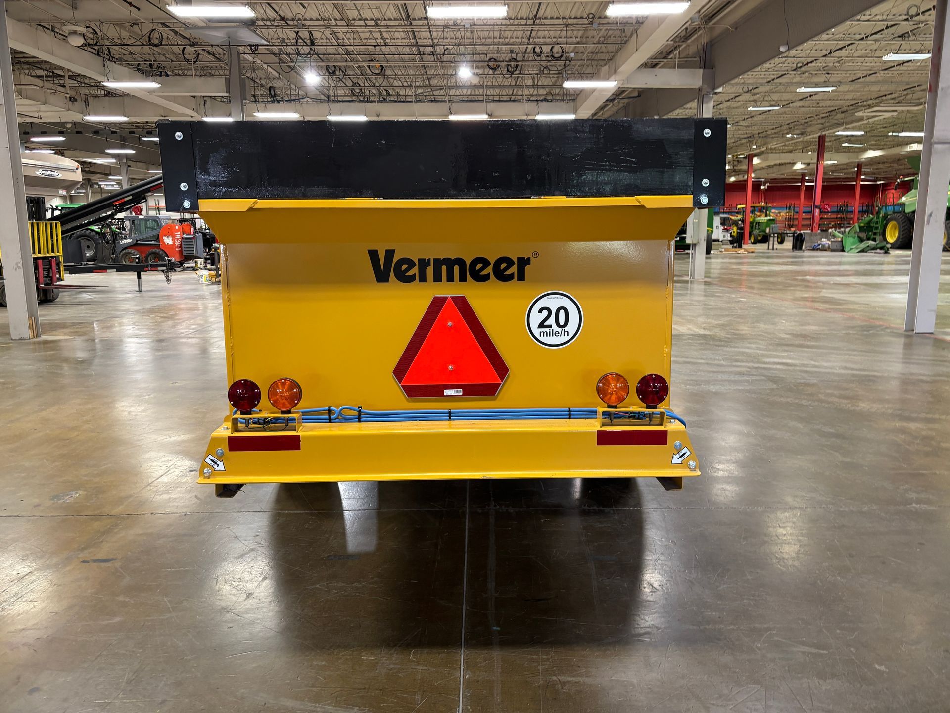 Yellow Vermeer spreader, black top, with warning triangle and 20 km/h sign on the back, in a warehouse.