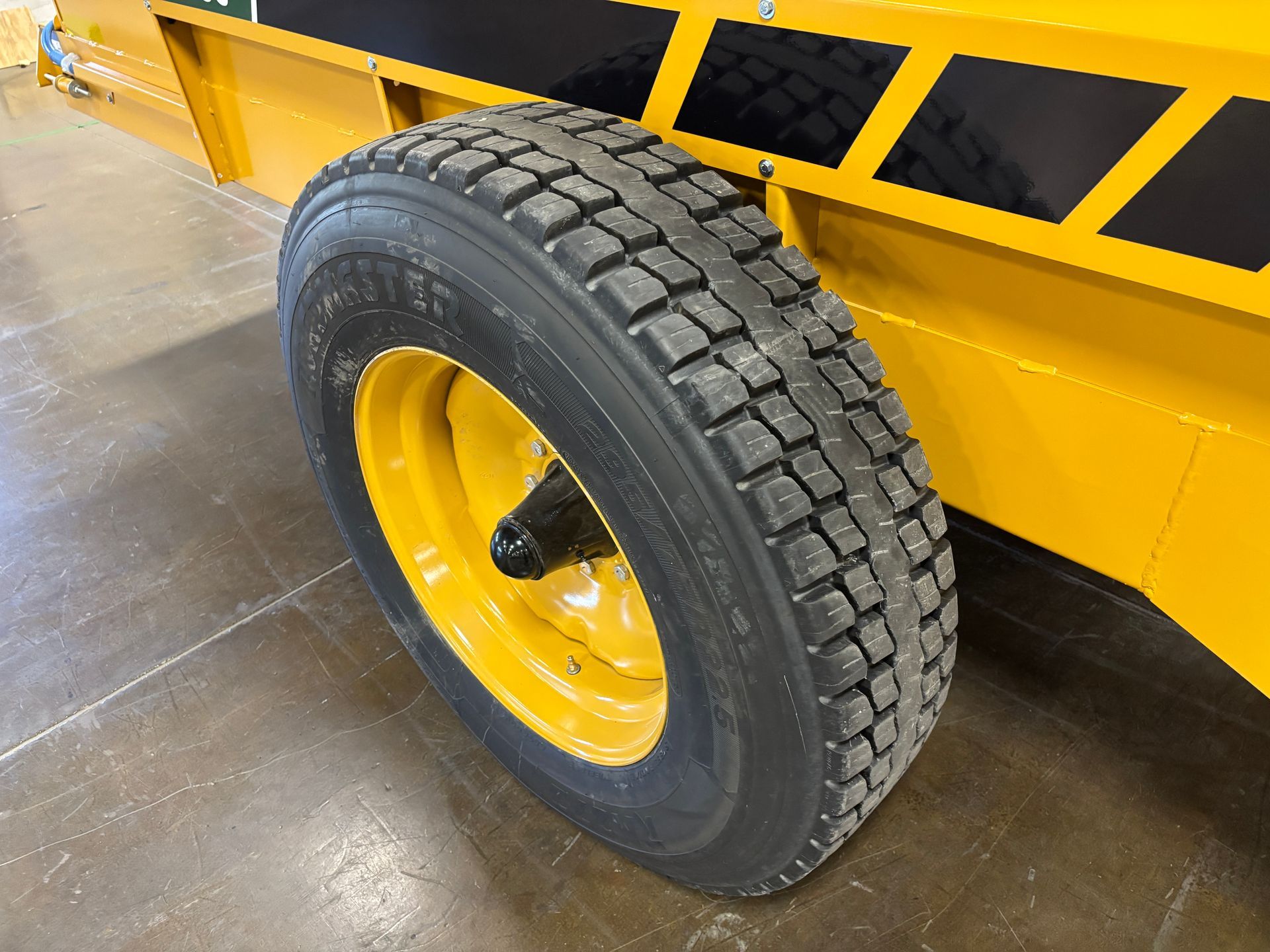 Yellow trailer wheel with a black tire on a gray surface.