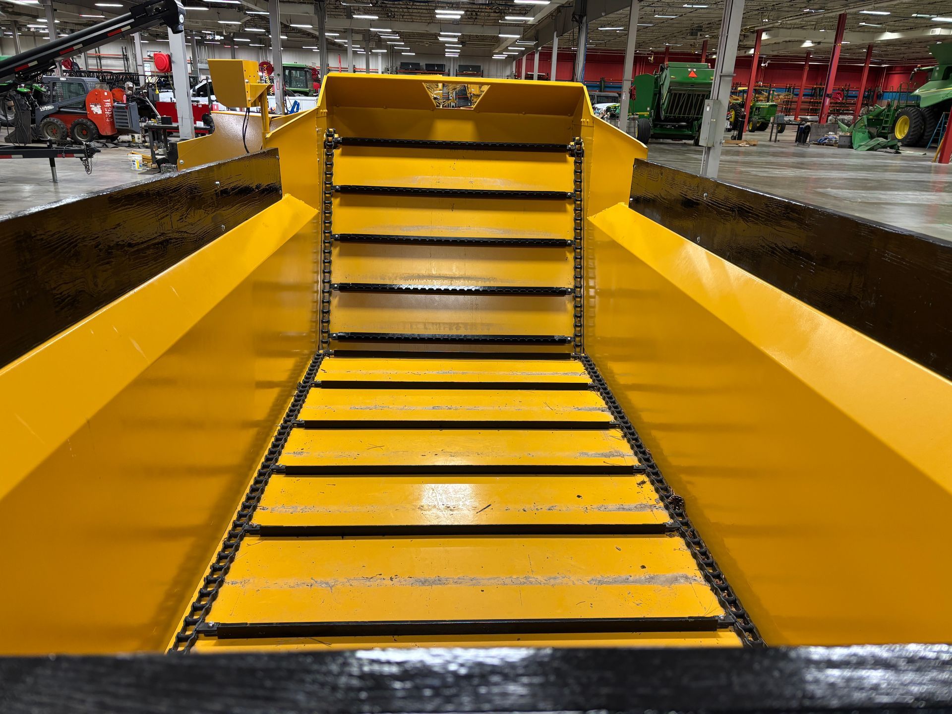 Yellow and black farm equipment bed, showing internal conveyor belt.