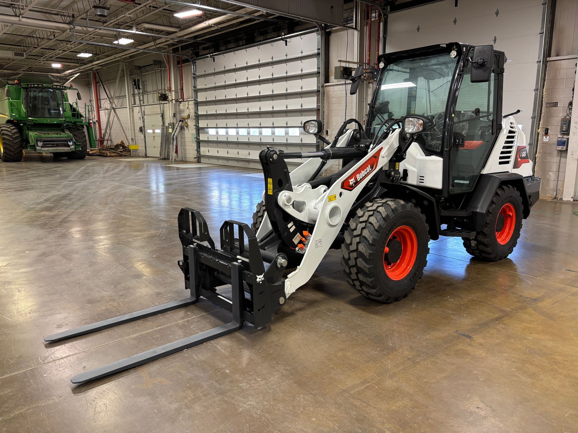 White and orange Bobcat loader with pallet forks in a warehouse.