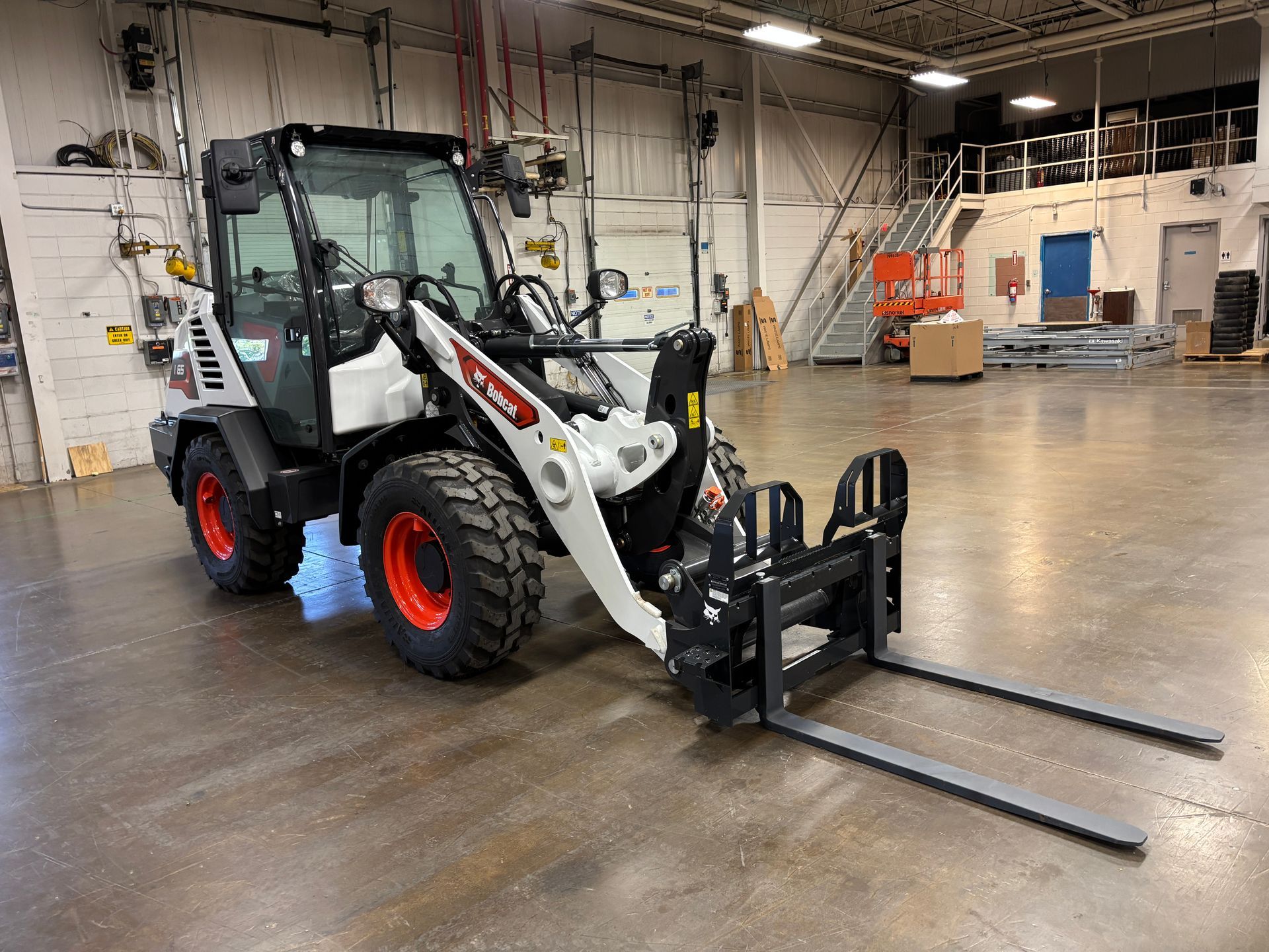 Bobcat compact wheel loader with fork attachment in an industrial setting.