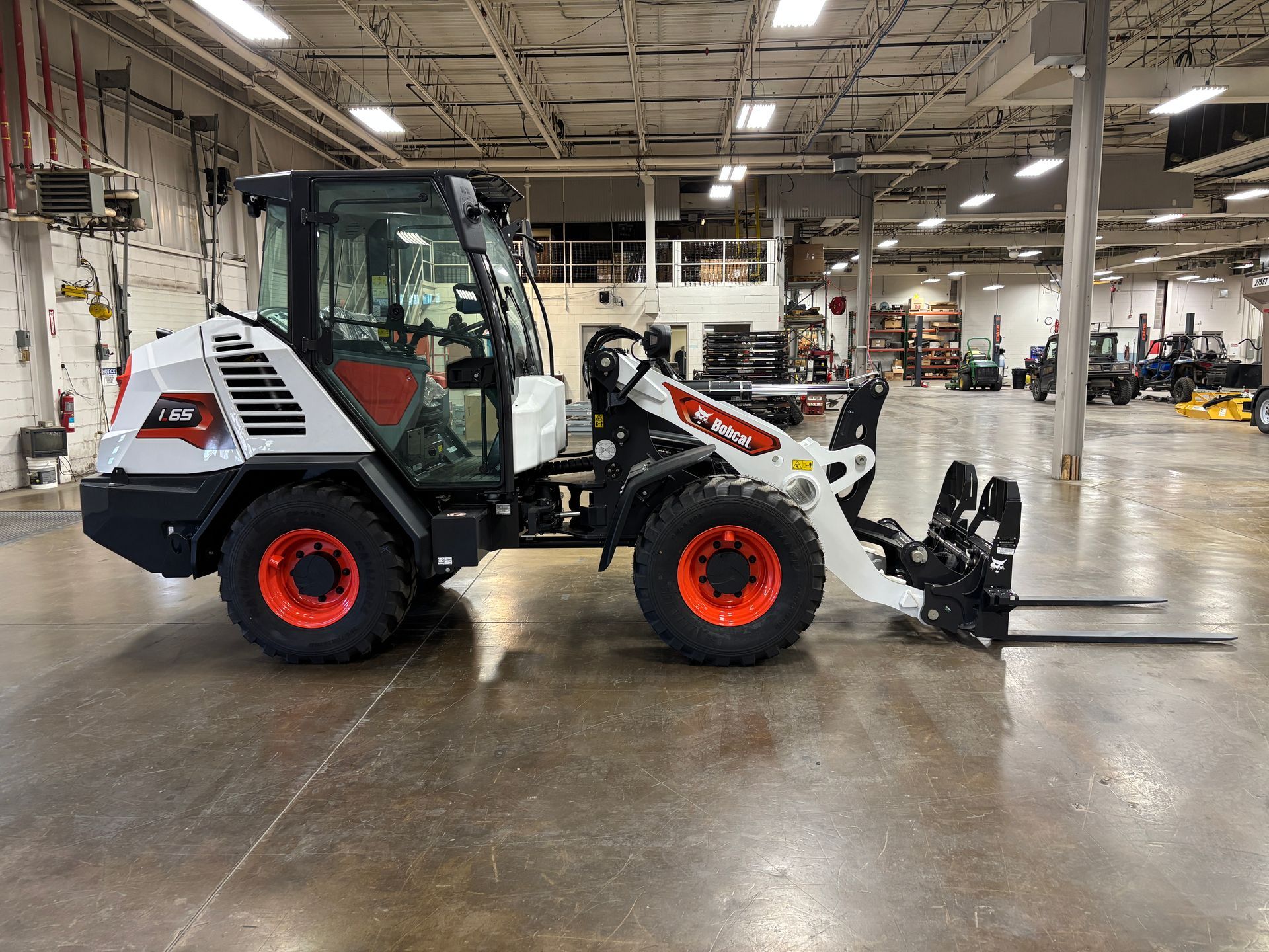 White and red Bobcat compact wheel loader with forks inside a warehouse.