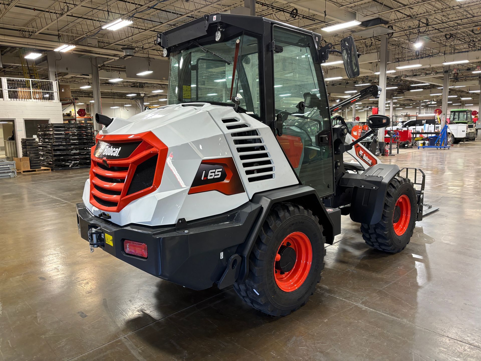 White and orange Bobcat compact wheel loader with cab in a warehouse setting.