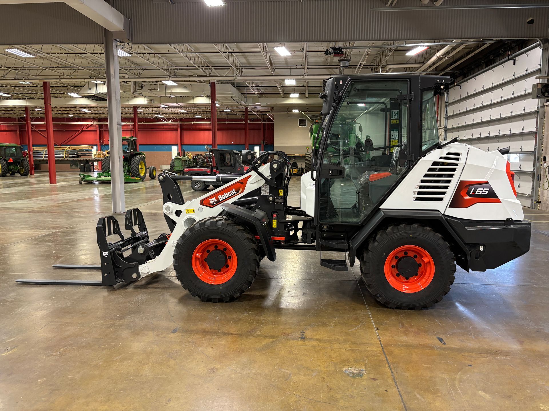 Bobcat compact loader with forks, white and orange, inside a warehouse.