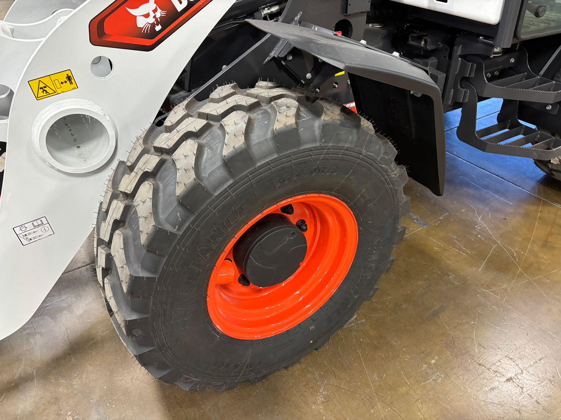 Close-up of a Bobcat wheel. The tire has a deep tread. The rim is bright orange.