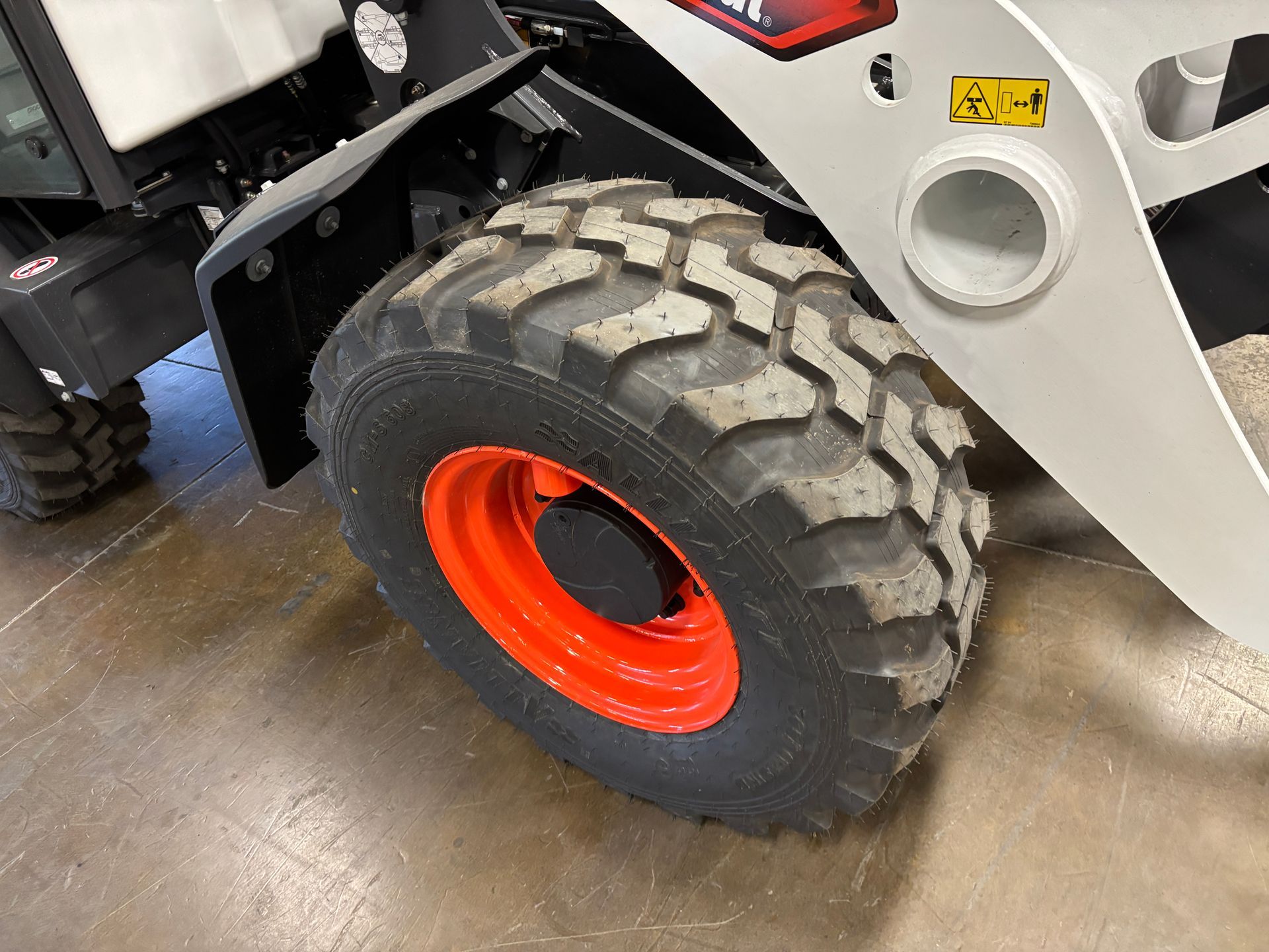 Bobcat skid steer wheel with black tire and orange rim.