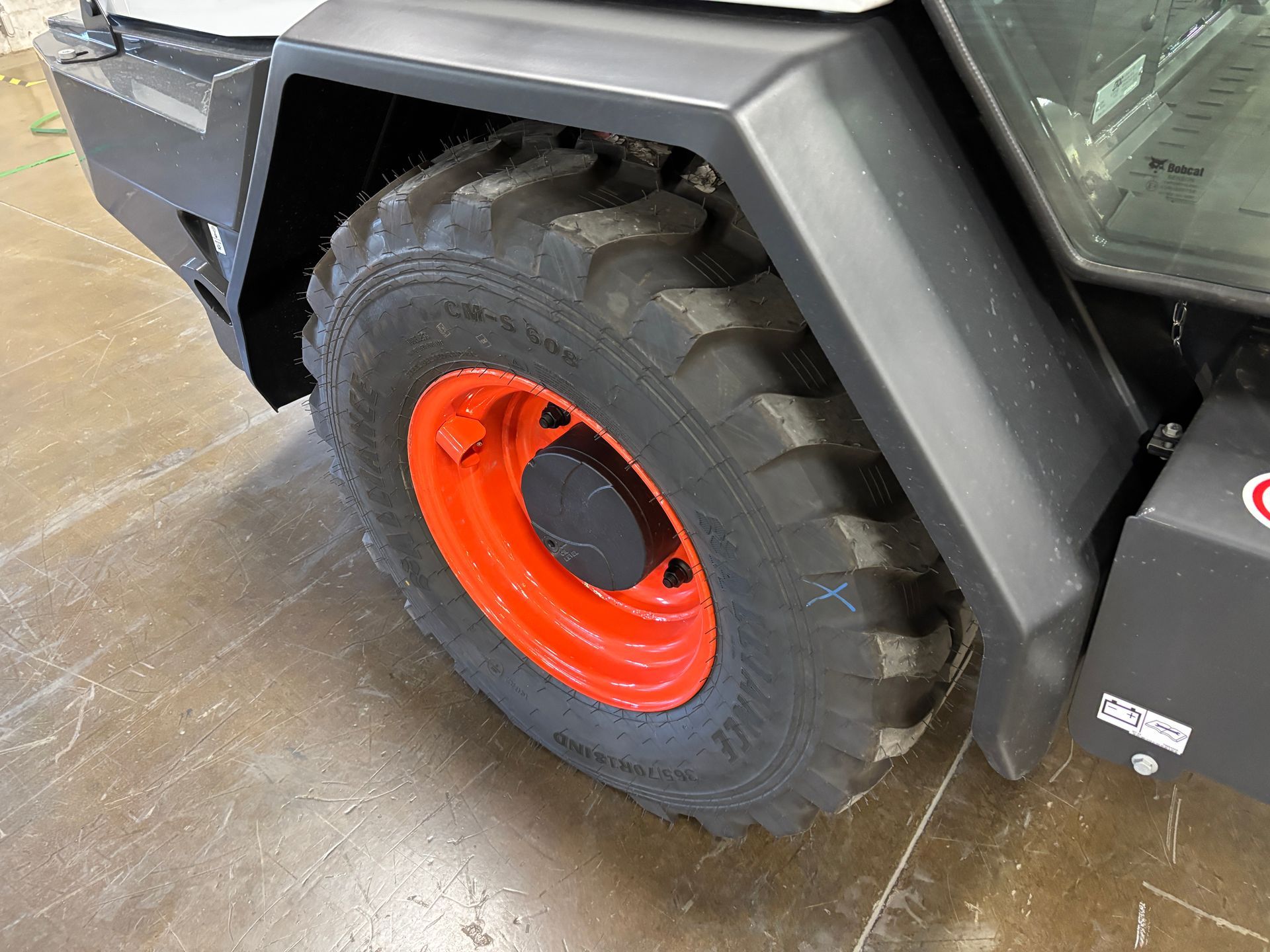 A close-up of a Bobcat wheel. The tire is black, and the rim is orange. The fender is black.
