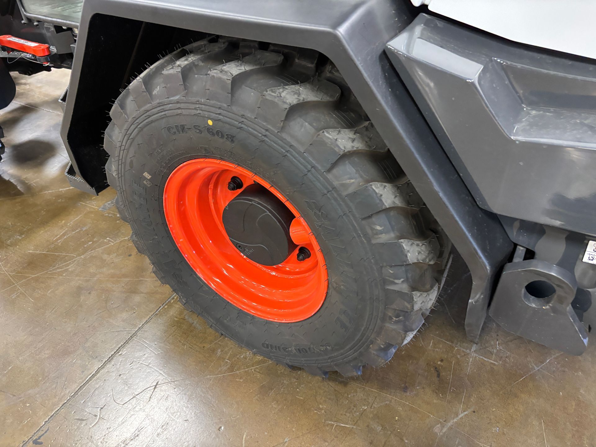 Close-up of a large, black tire with an orange wheel on a gray machine, set on a tan floor.
