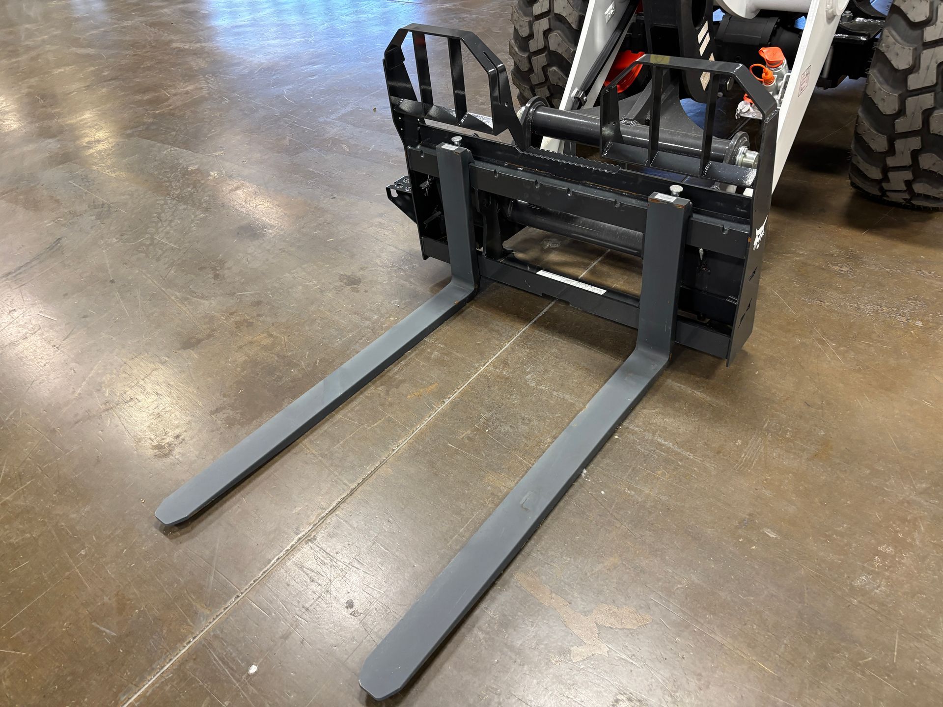 Forklift forks extending from a black and white tractor on a concrete floor.