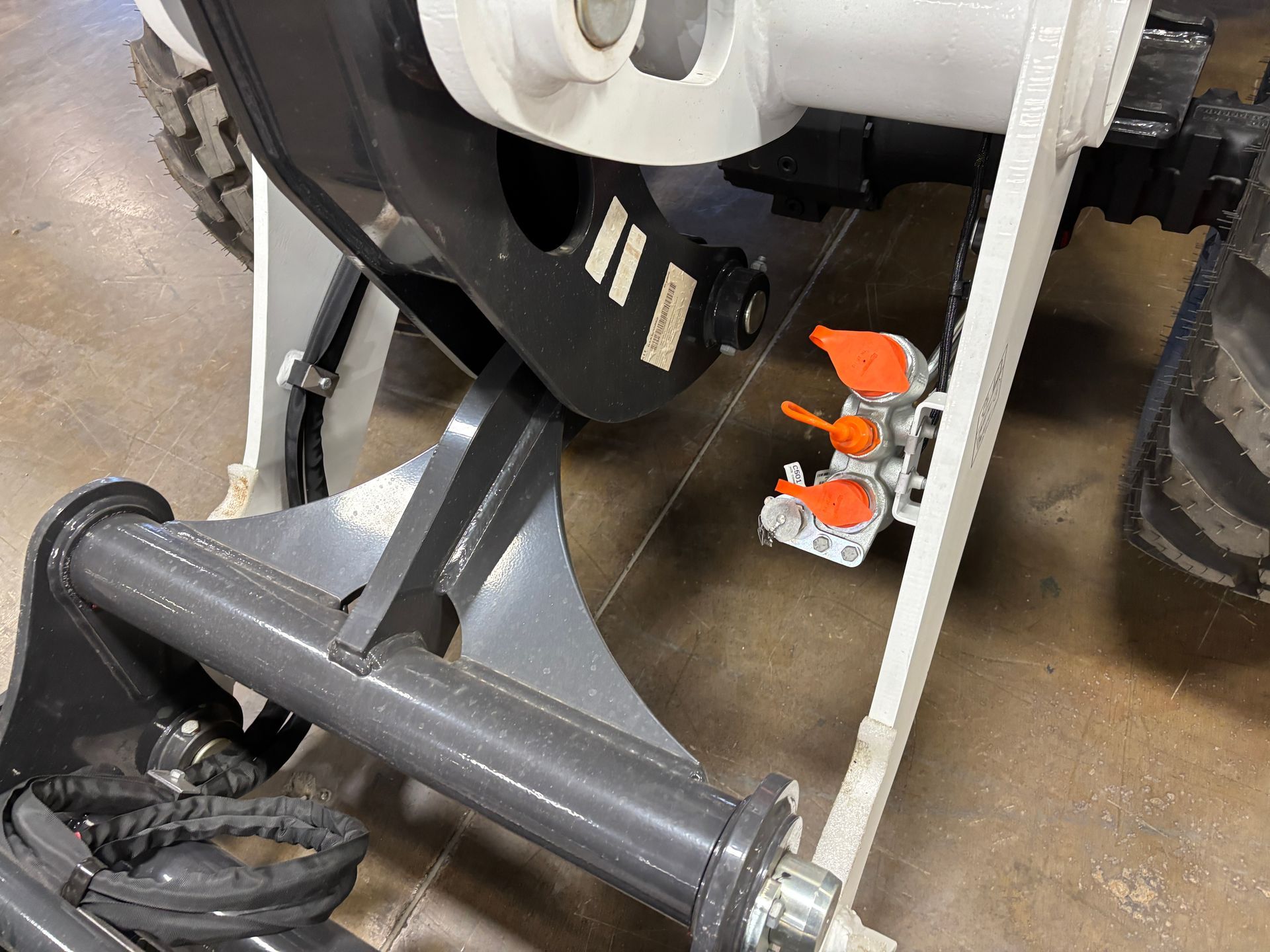 Close-up of a skid steer coupler with hydraulic lines and a gray and white arm and a tire.