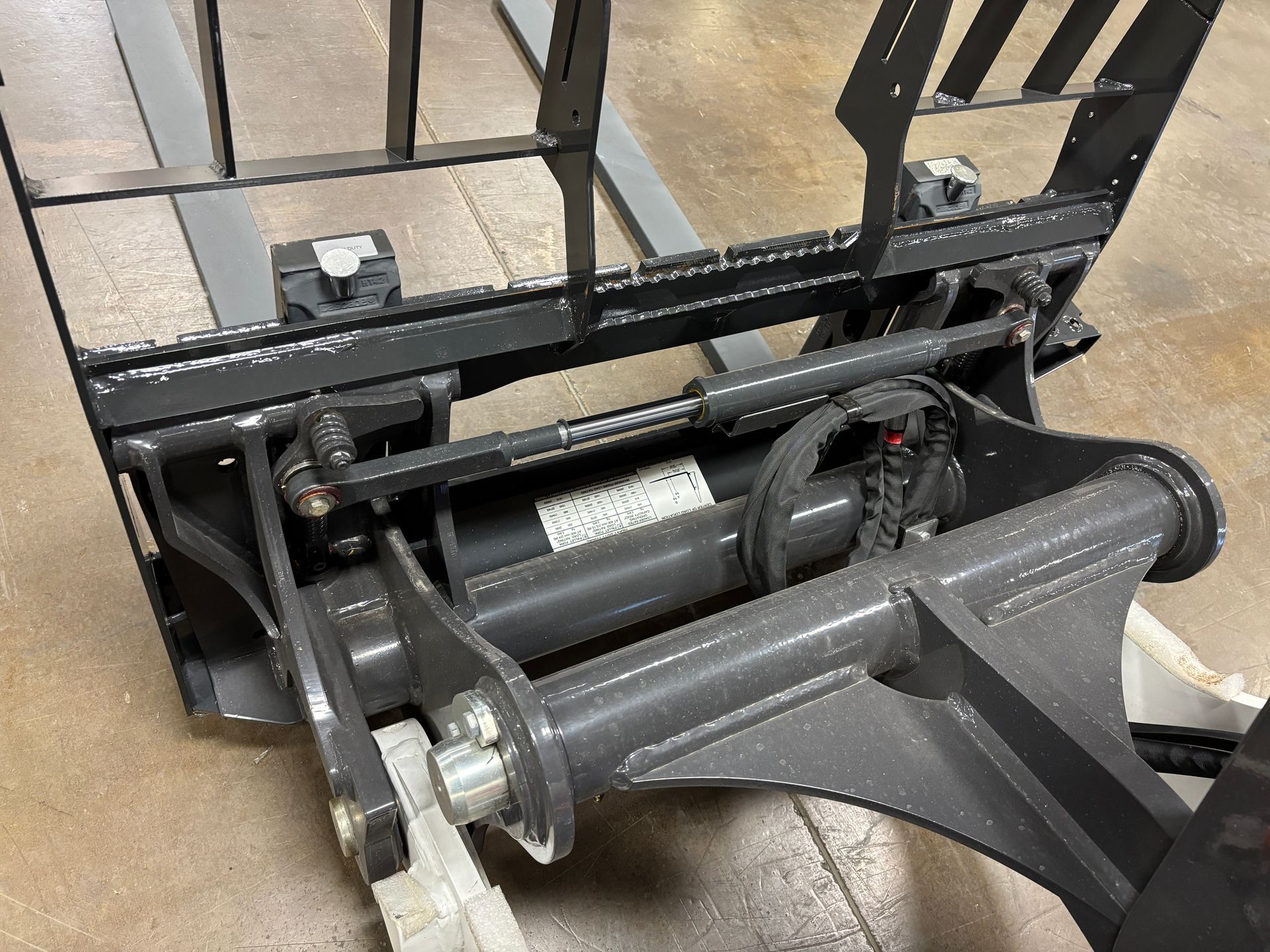 Forklift attachment, gray metal, with hydraulic cylinder and forks.
