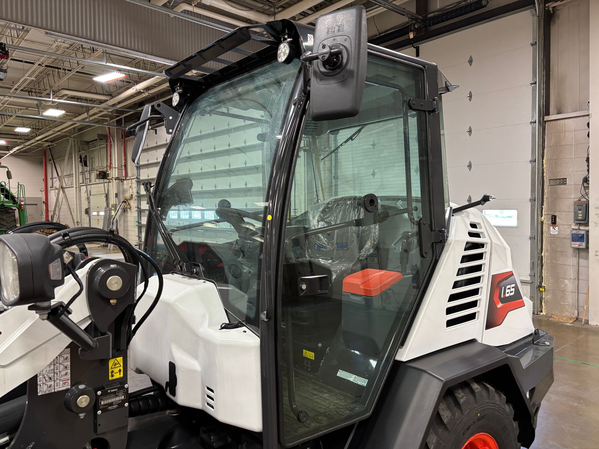 White and black Bobcat loader cab with glass windows and black trim inside a building.