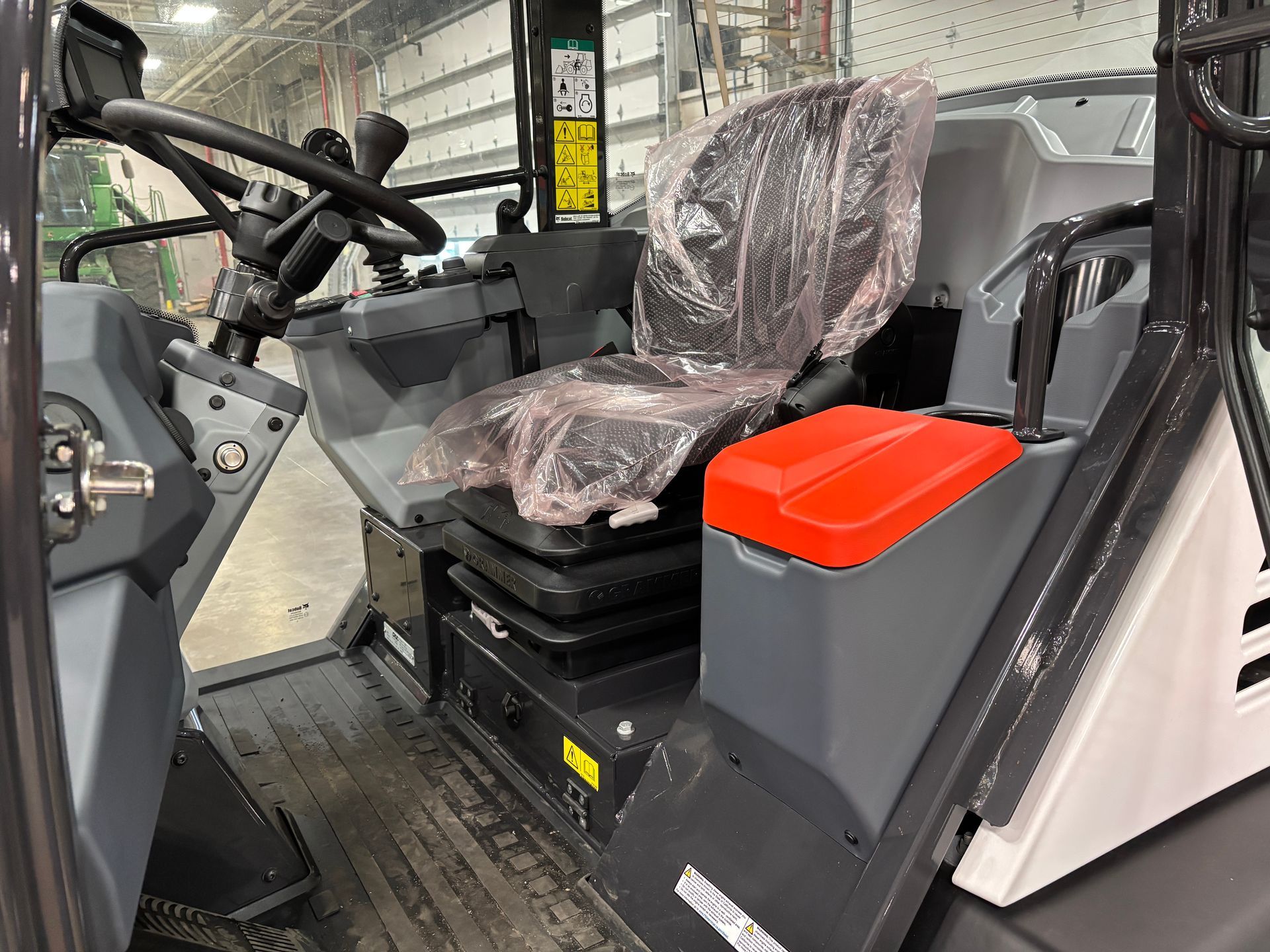 Interior of a utility vehicle: driver's seat with plastic cover, steering wheel, and a red-topped storage box.
