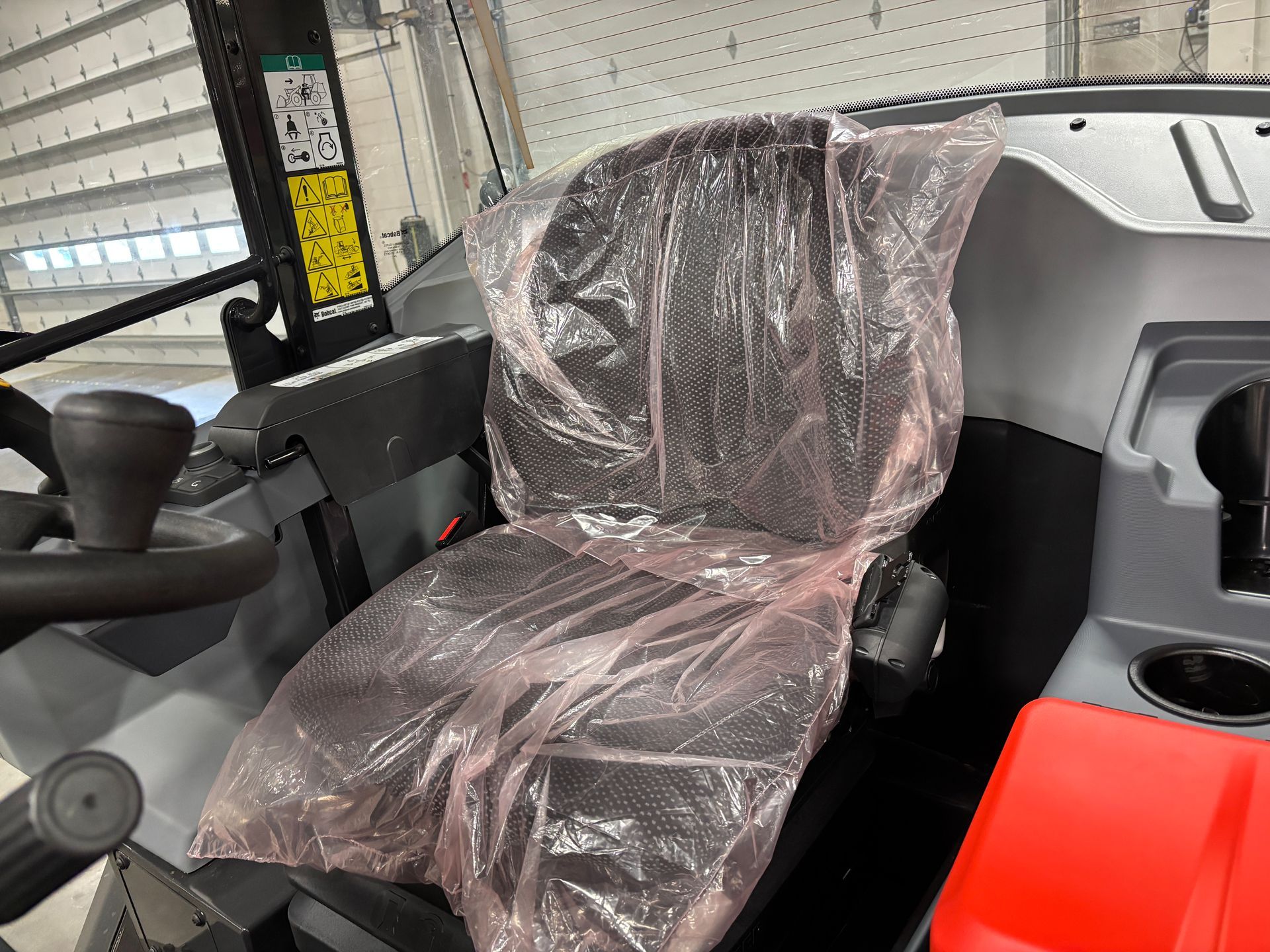 A tractor cab interior. The seat is covered in clear plastic.