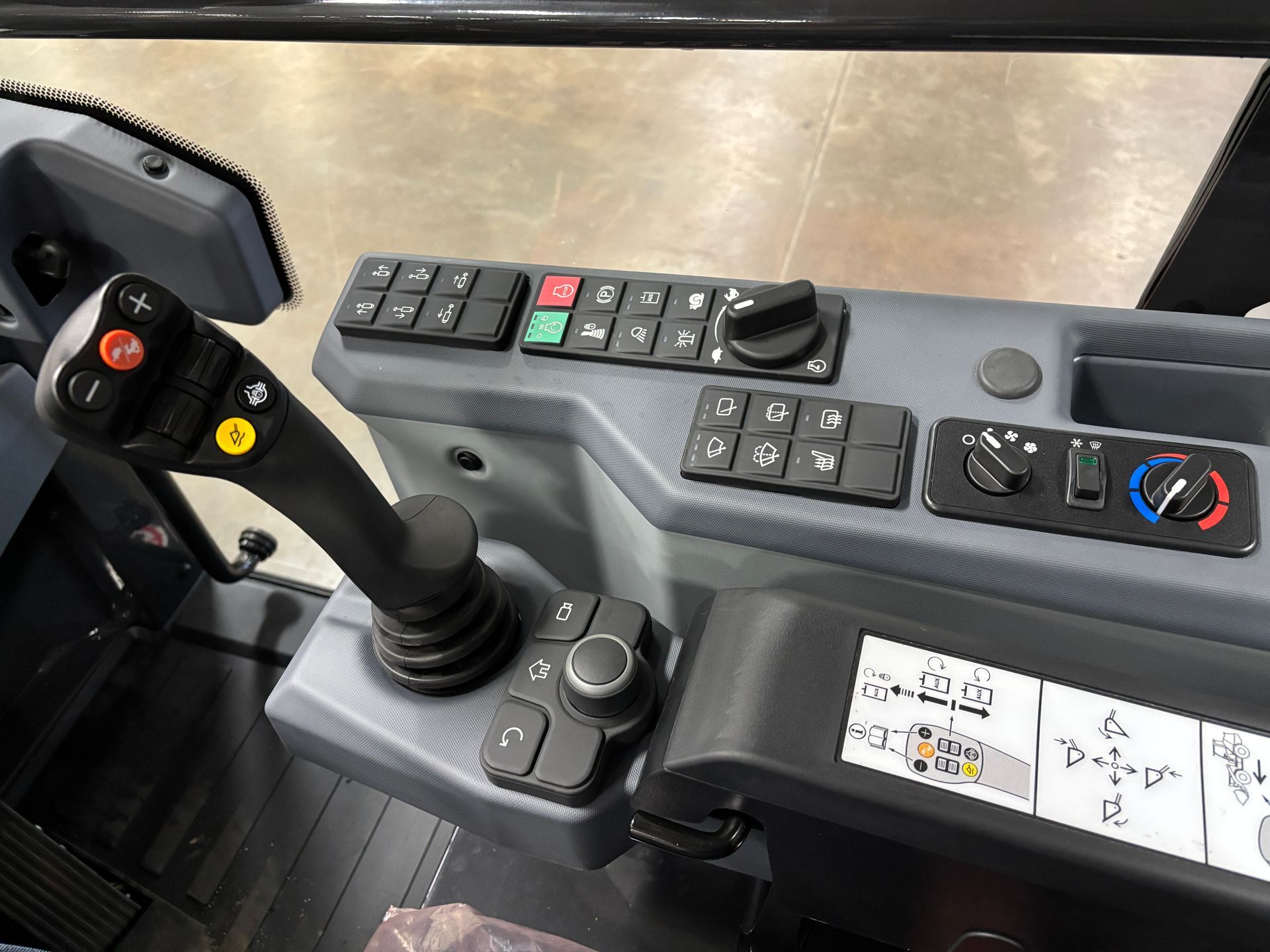Control panel in a construction vehicle with a joystick, buttons, and switches, and a control knob.