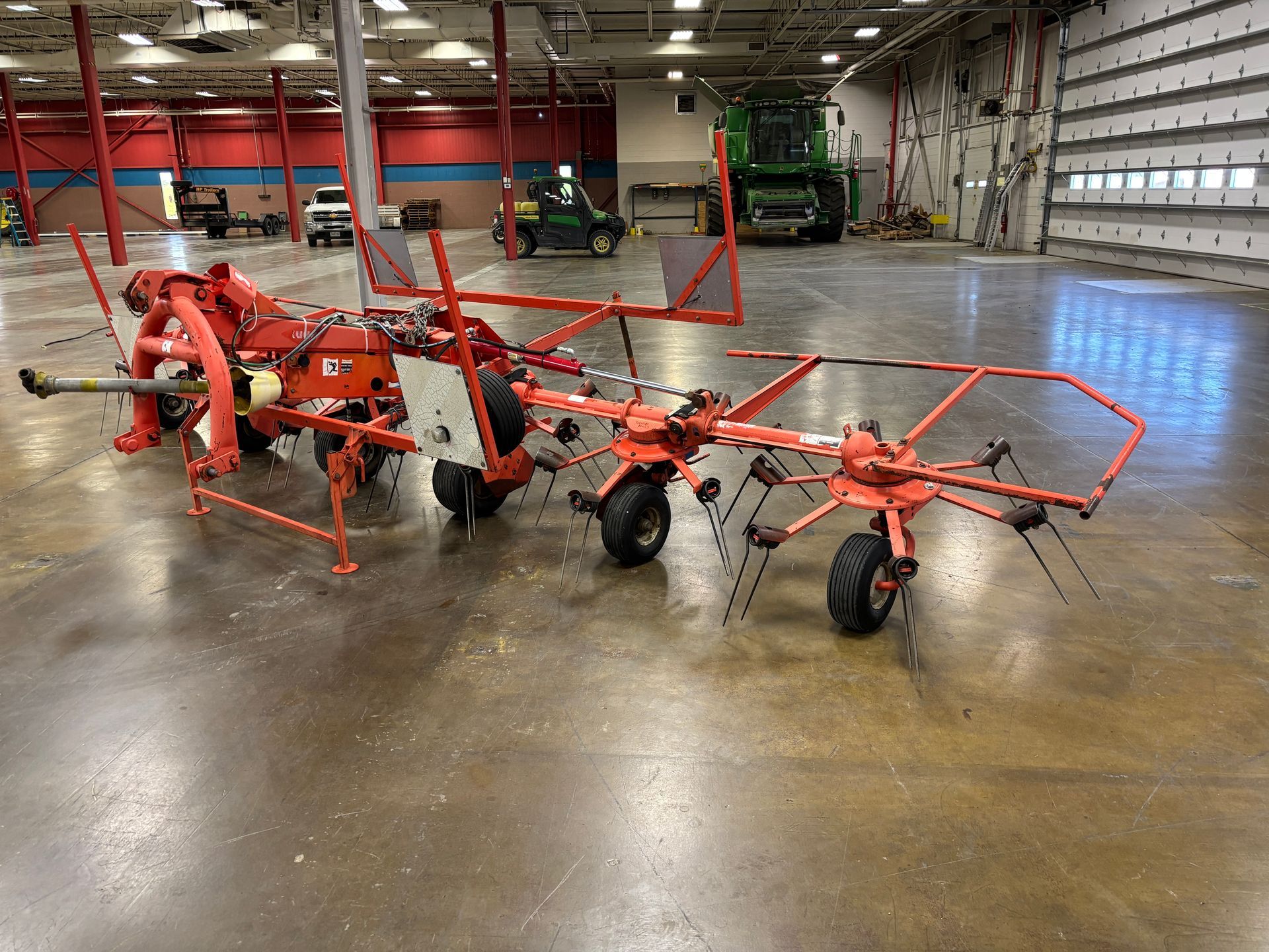 A red agricultural hay rake sits on a concrete floor inside a large building.