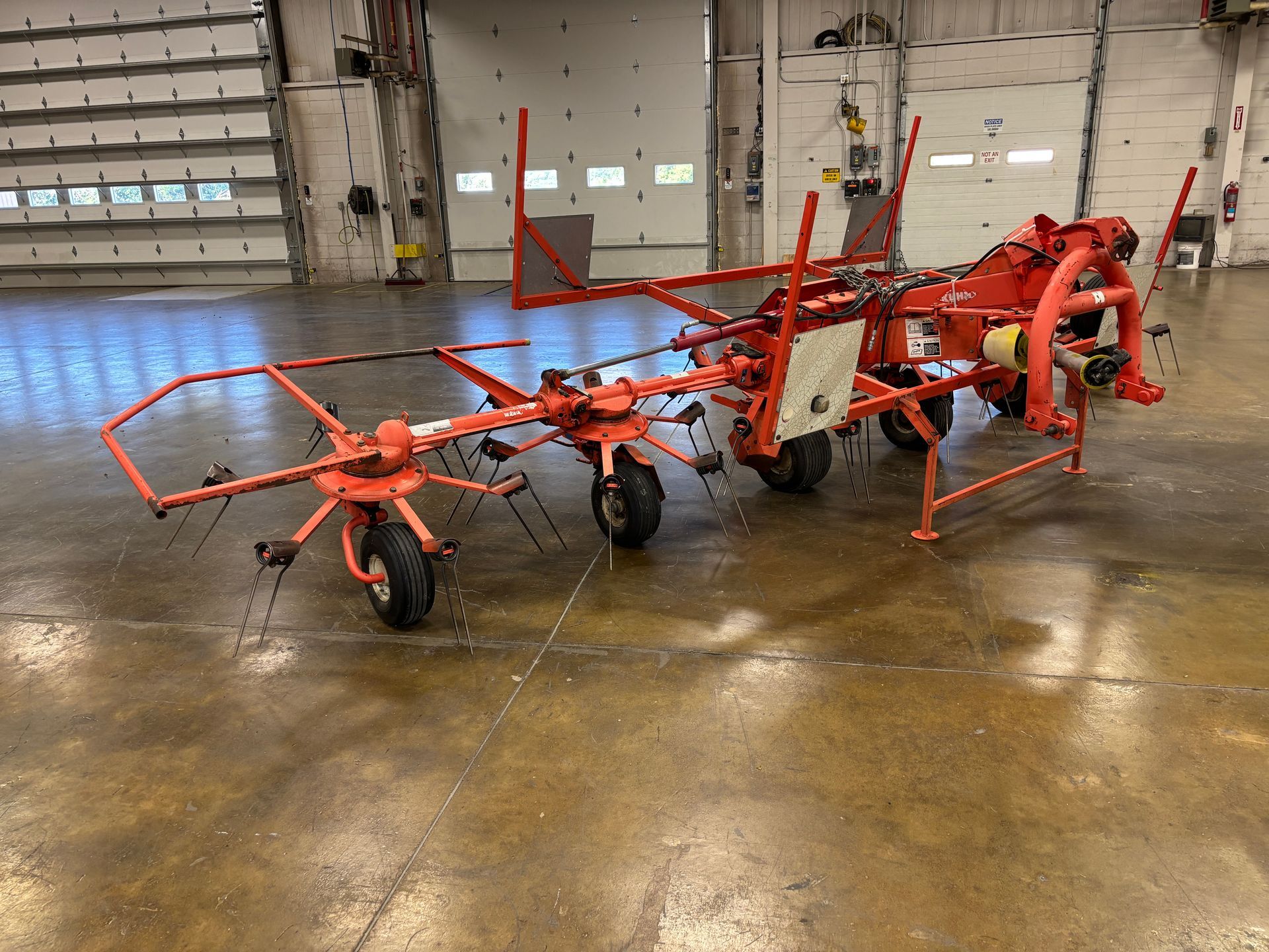 Orange Kuhn hay rake on a glossy concrete floor in a warehouse.