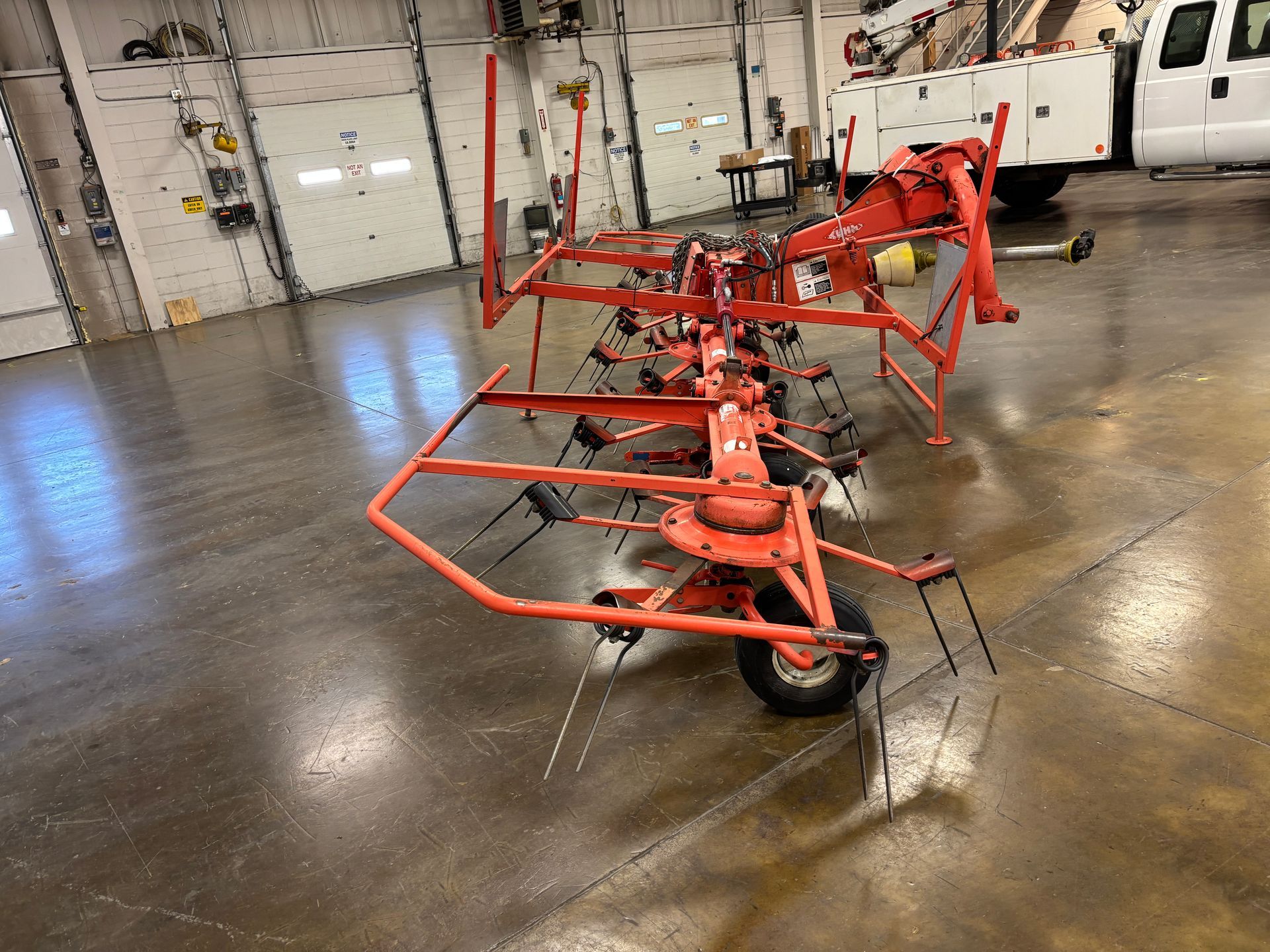 Orange farm hay rake on a concrete floor in a workshop.