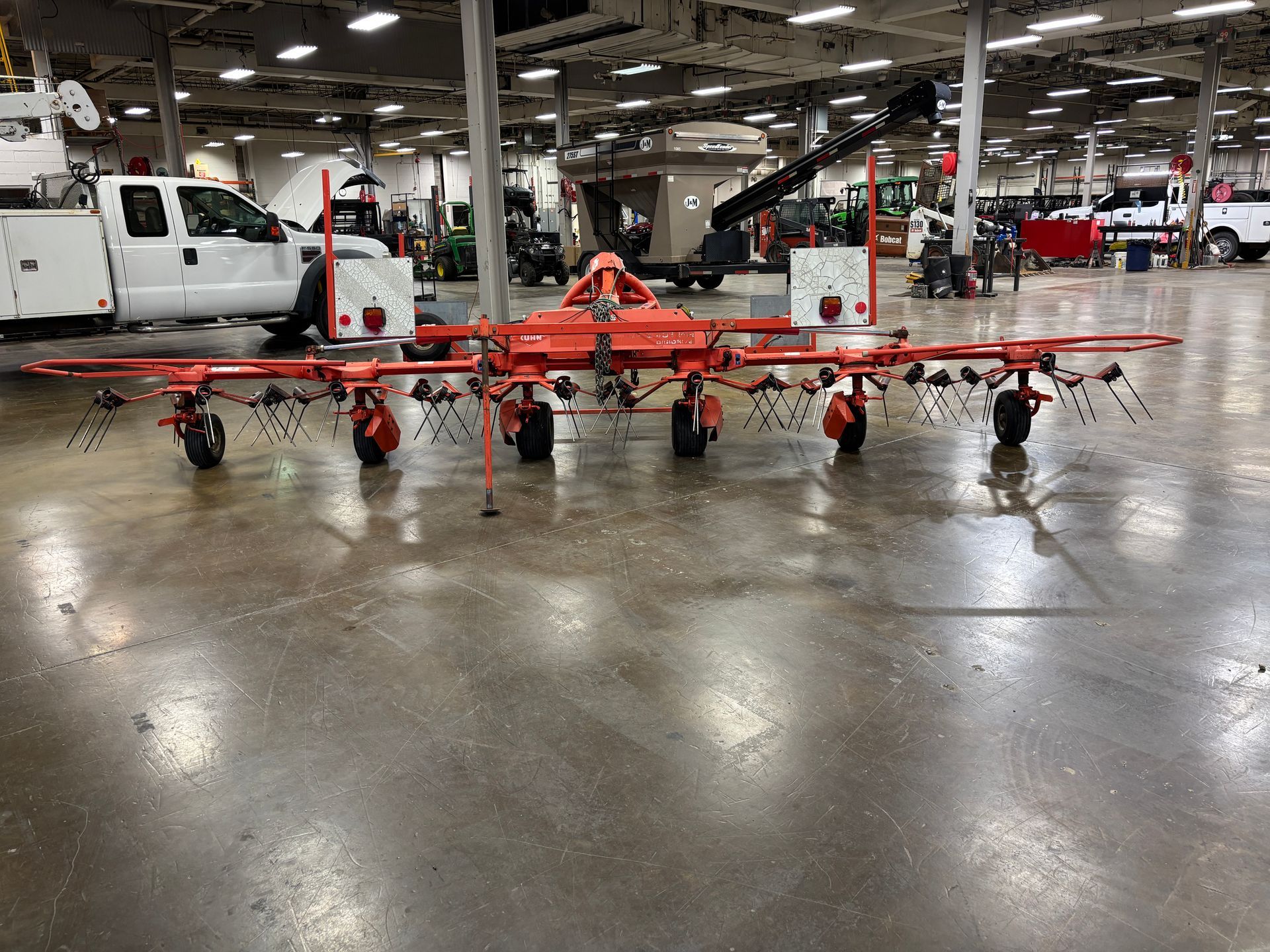 Orange agricultural hay rake on a gray concrete floor in a warehouse.