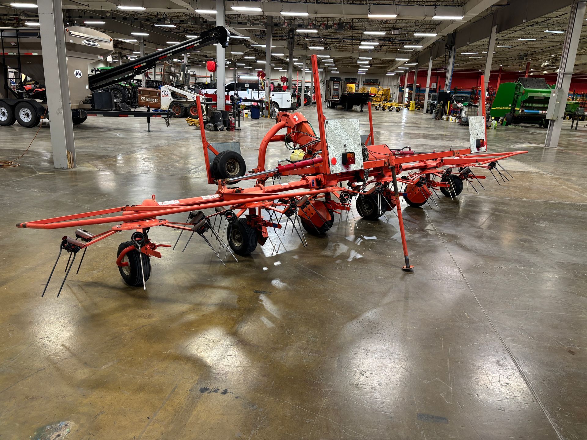 Red farm hay rake on a glossy concrete floor inside a large building.