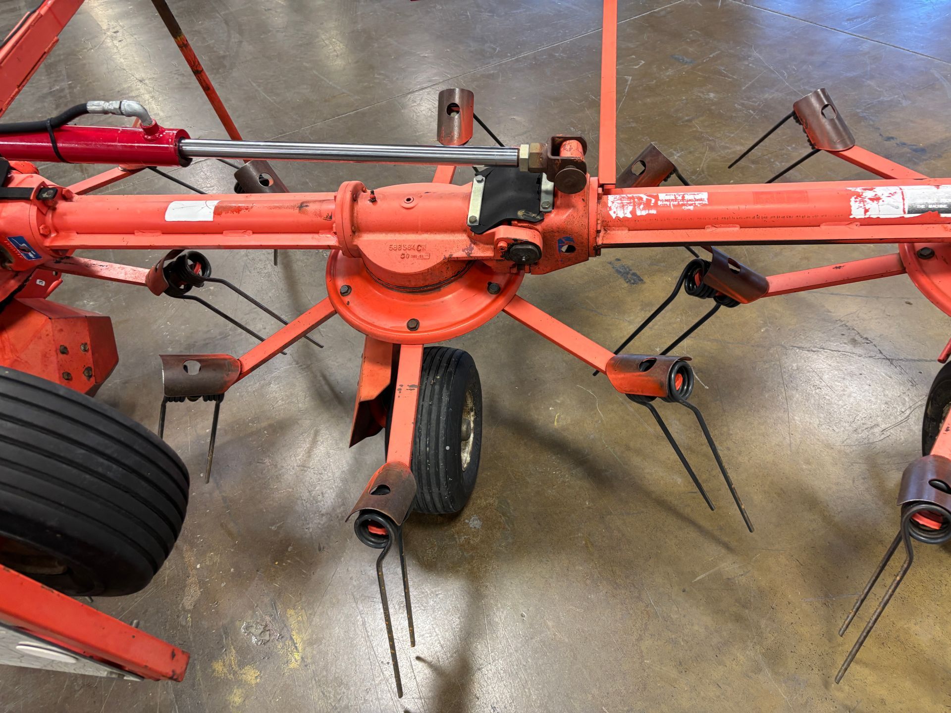 Orange hay rake, with black tines, wheels, and a hydraulic cylinder.