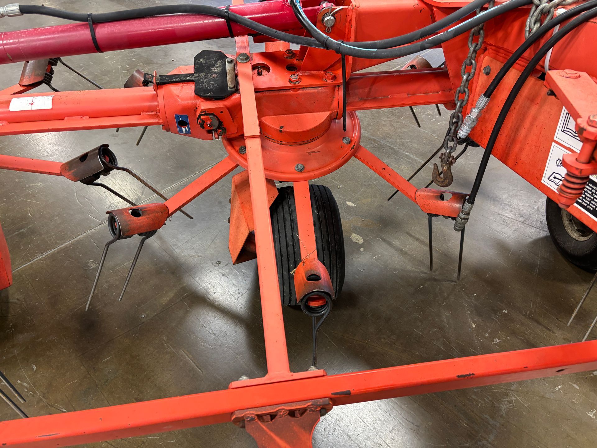 Orange hay rake machine with black tires and metal tines, viewed from above.