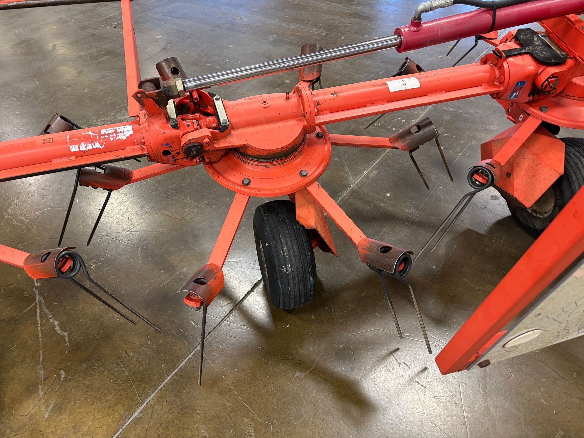 An orange hay rake with tines and a black tire on a concrete floor.