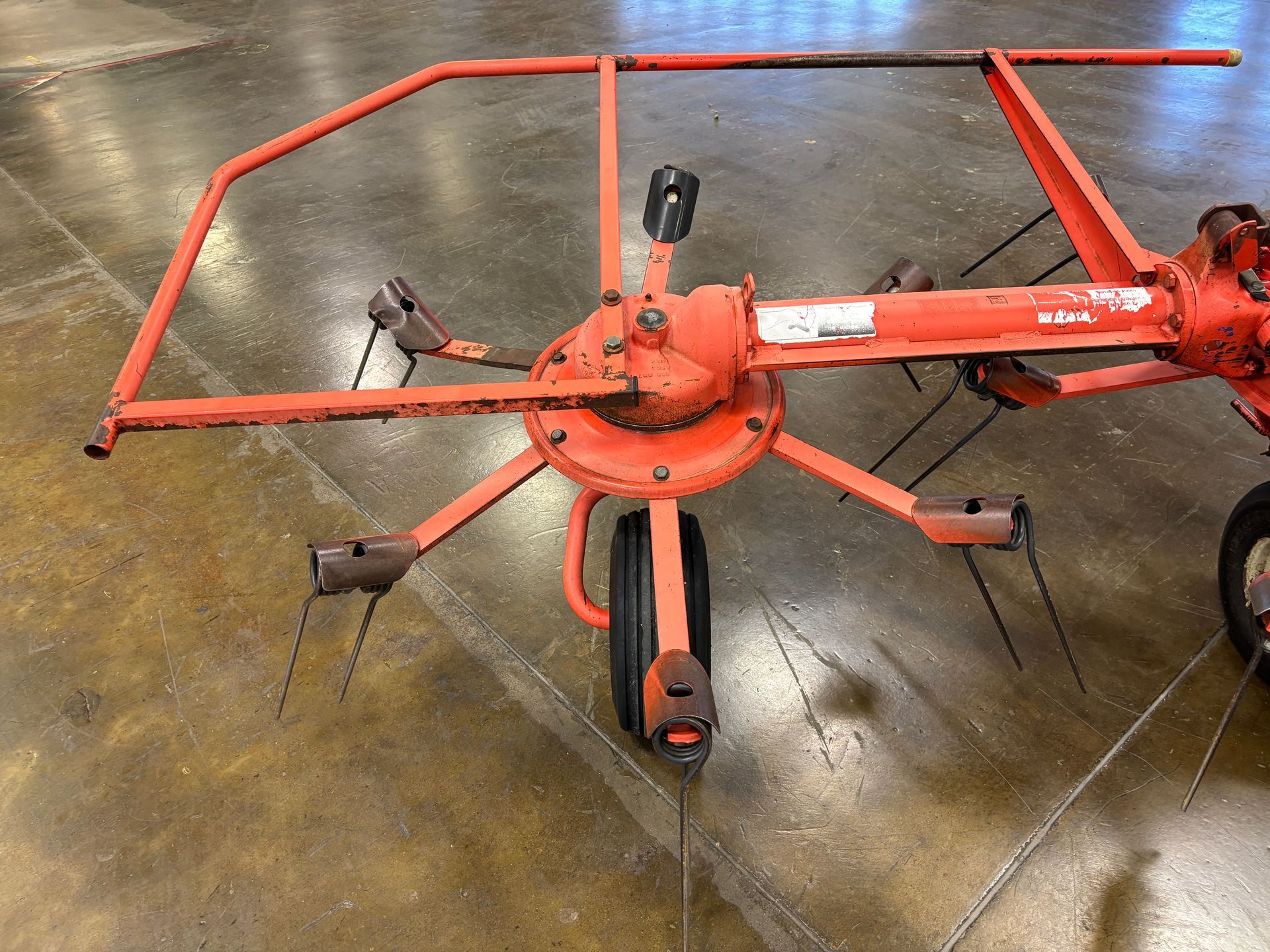 Orange farm hay rake on a concrete floor.