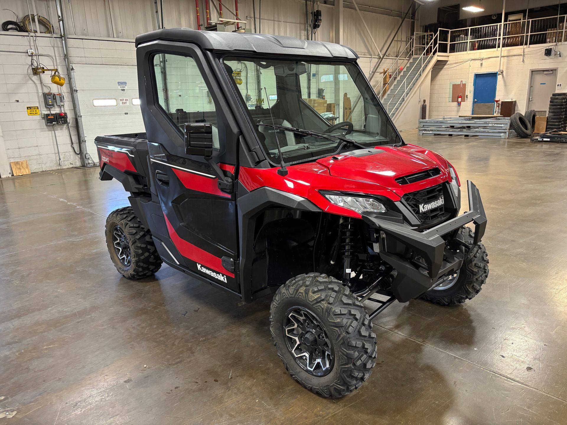 Red and black Kawasaki UTV with black roll cage and large tires.