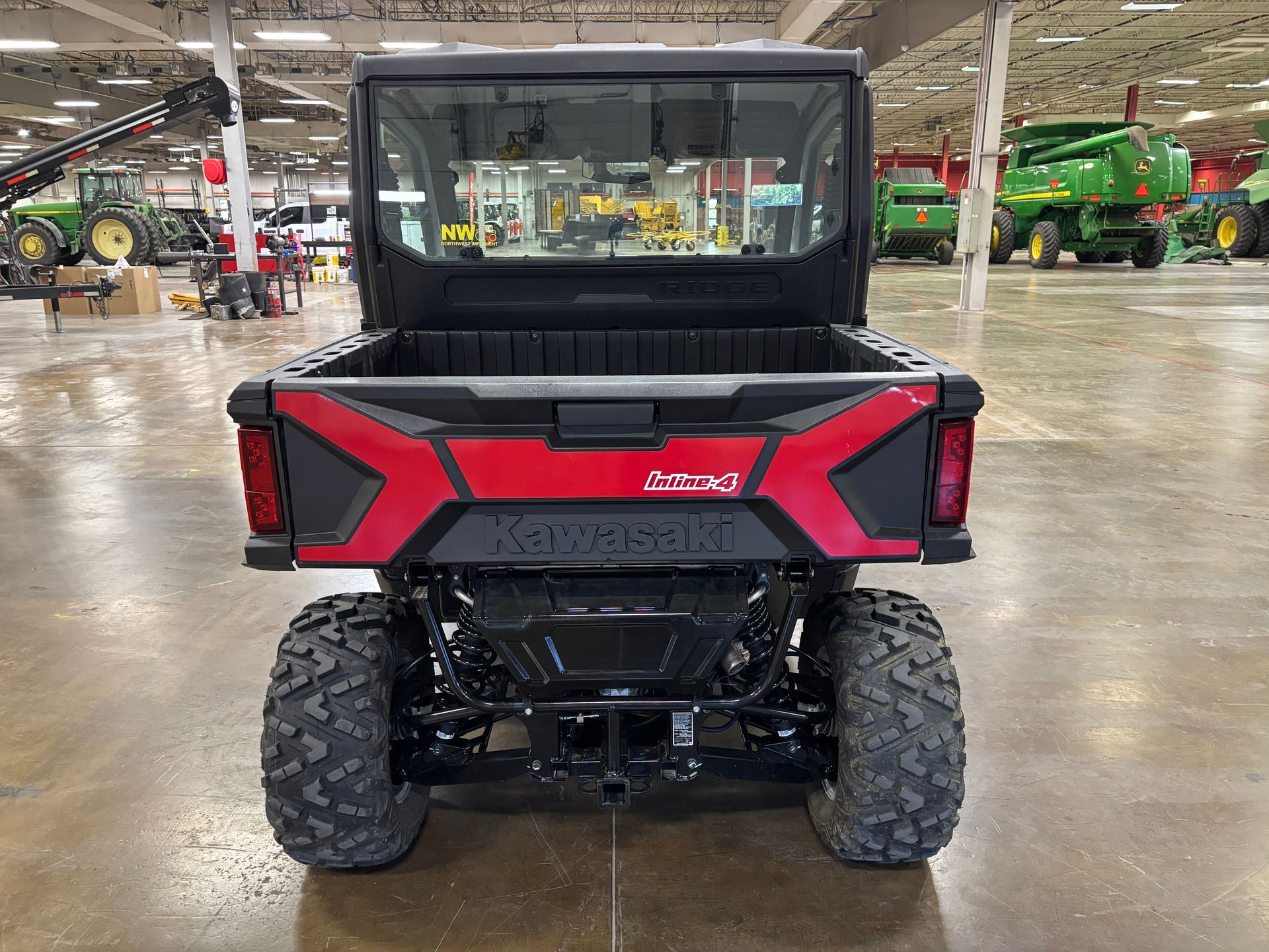 Red Kawasaki UTV rear view, black bed, large tires, indoor setting.