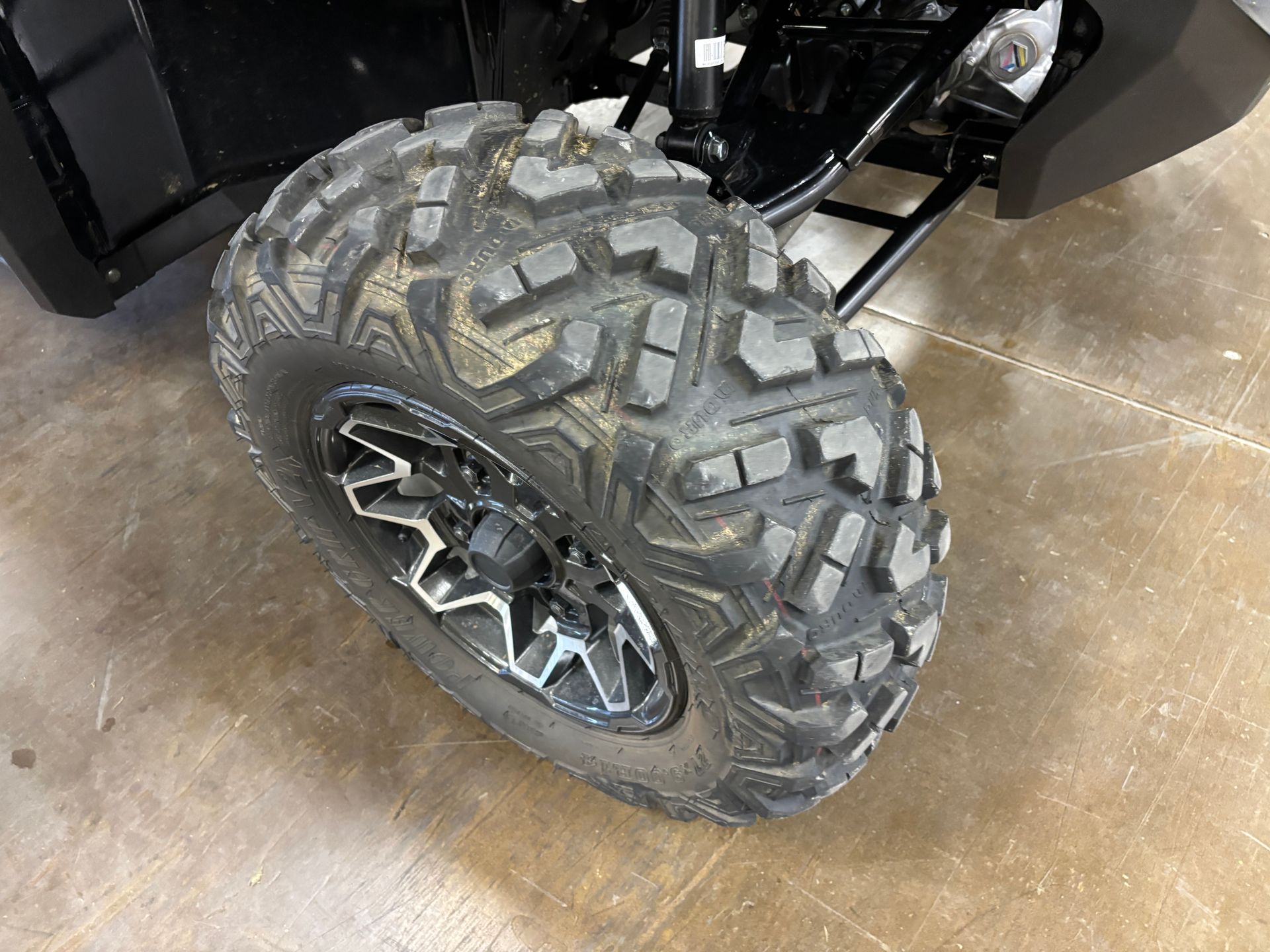 Black ATV tire with mud-covered tread, mounted on a shiny silver and black wheel.