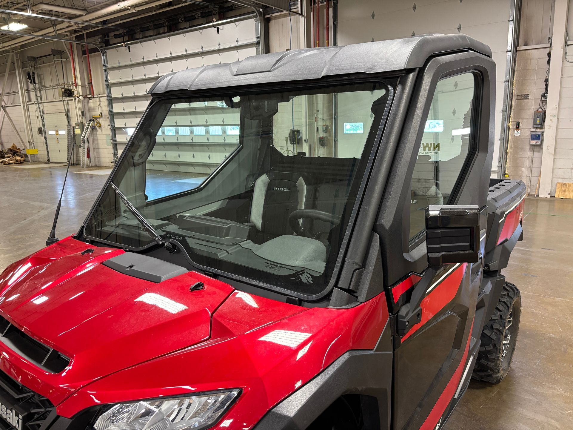 Red side-by-side UTV with a windshield, black roof, and side mirrors, parked inside a building.