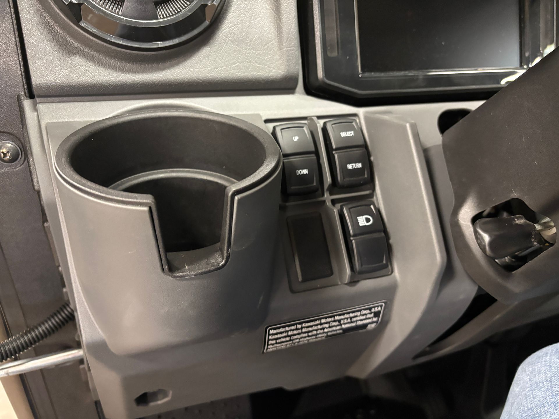 Dashboard of a vehicle with a cupholder, switches, and a digital display.