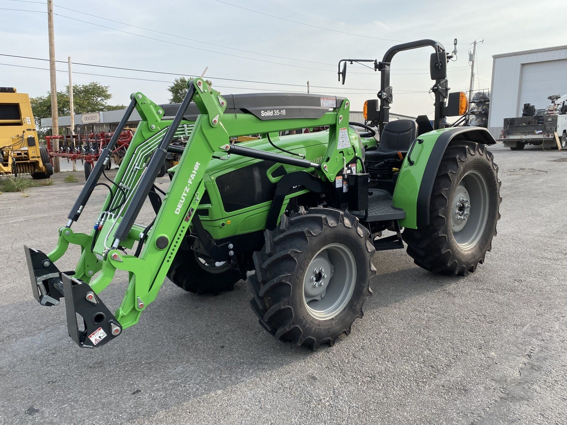 Green tractor with front loader on paved lot.