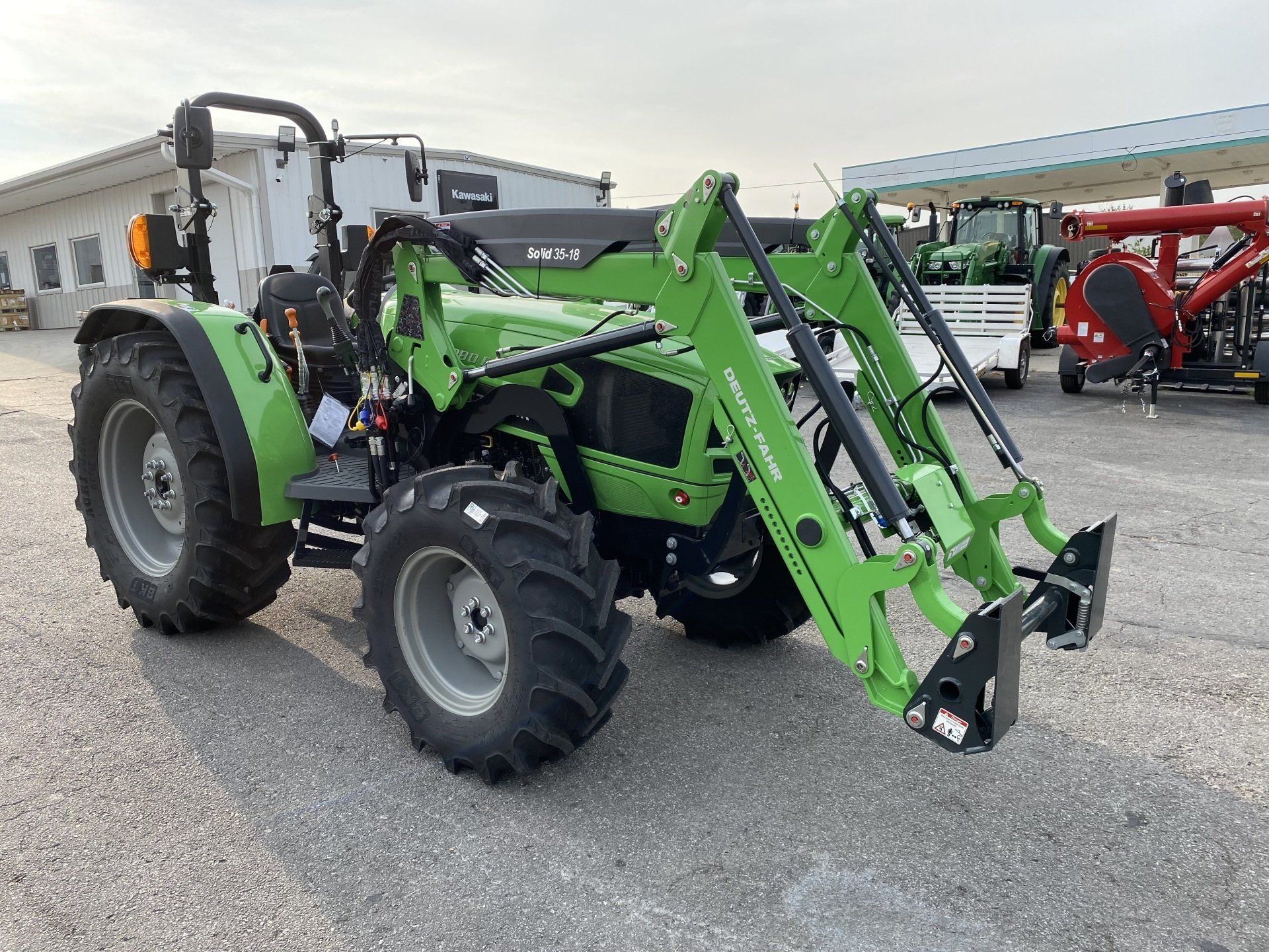 Green tractor with front loader parked outside a building.