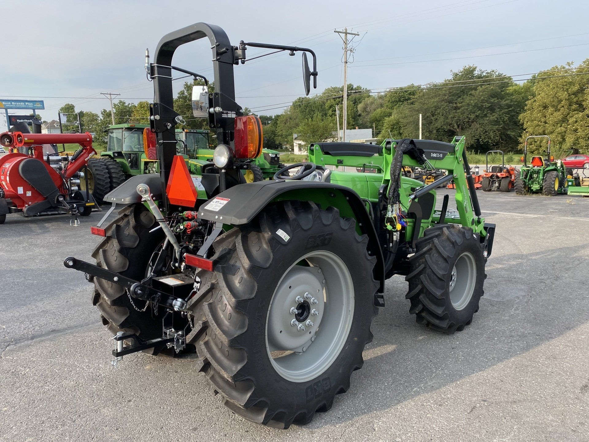 Green tractor with large tires, parked on pavement.  Rear view, visible roll bar and loader arm.