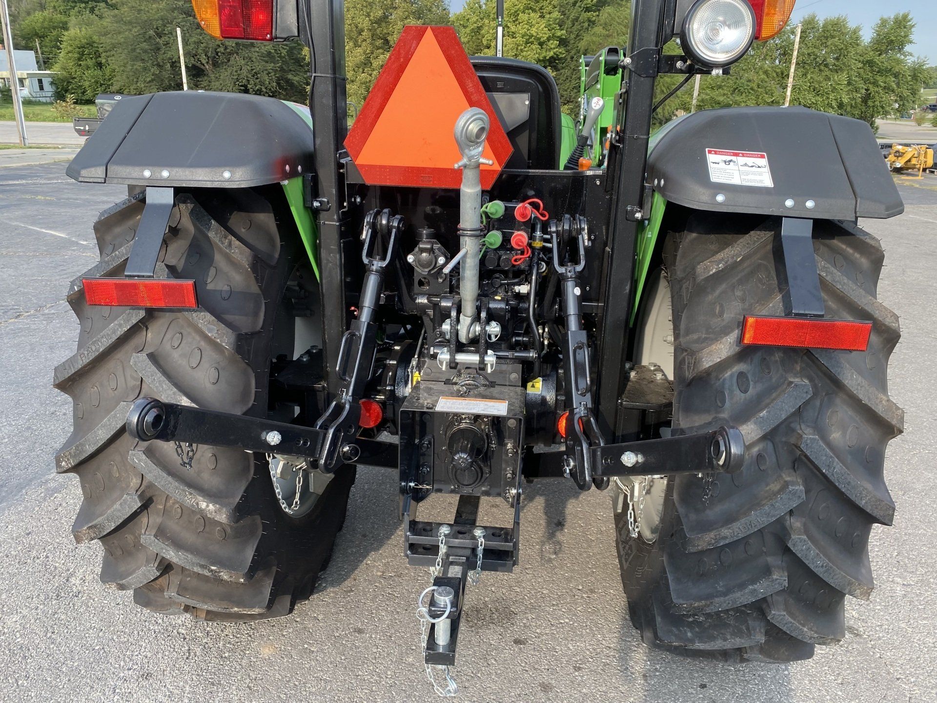 Rear view of a green tractor with large tires, orange safety triangle, and hitch.
