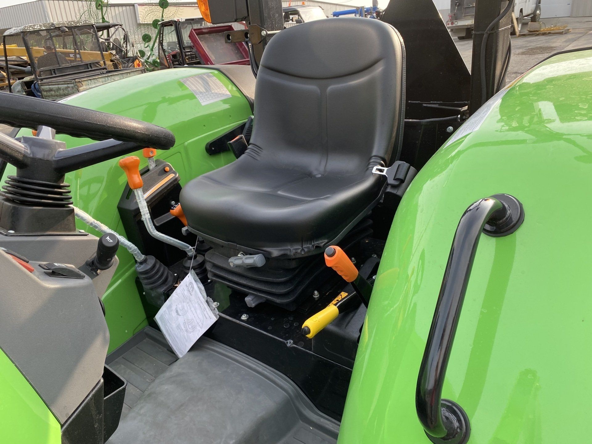Black tractor seat in a green tractor cab, with orange and yellow levers.