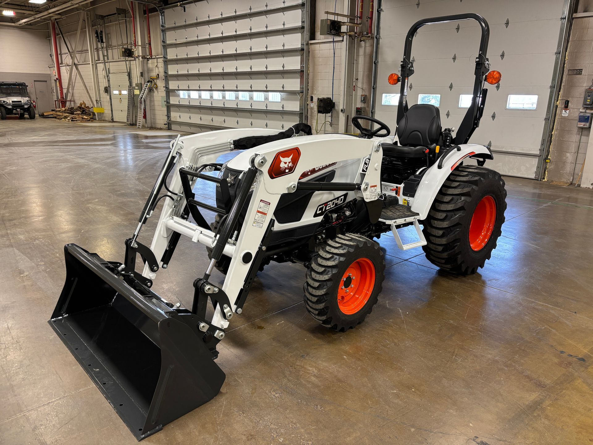 White Bobcat tractor with a front loader and orange wheels. Inside a garage.