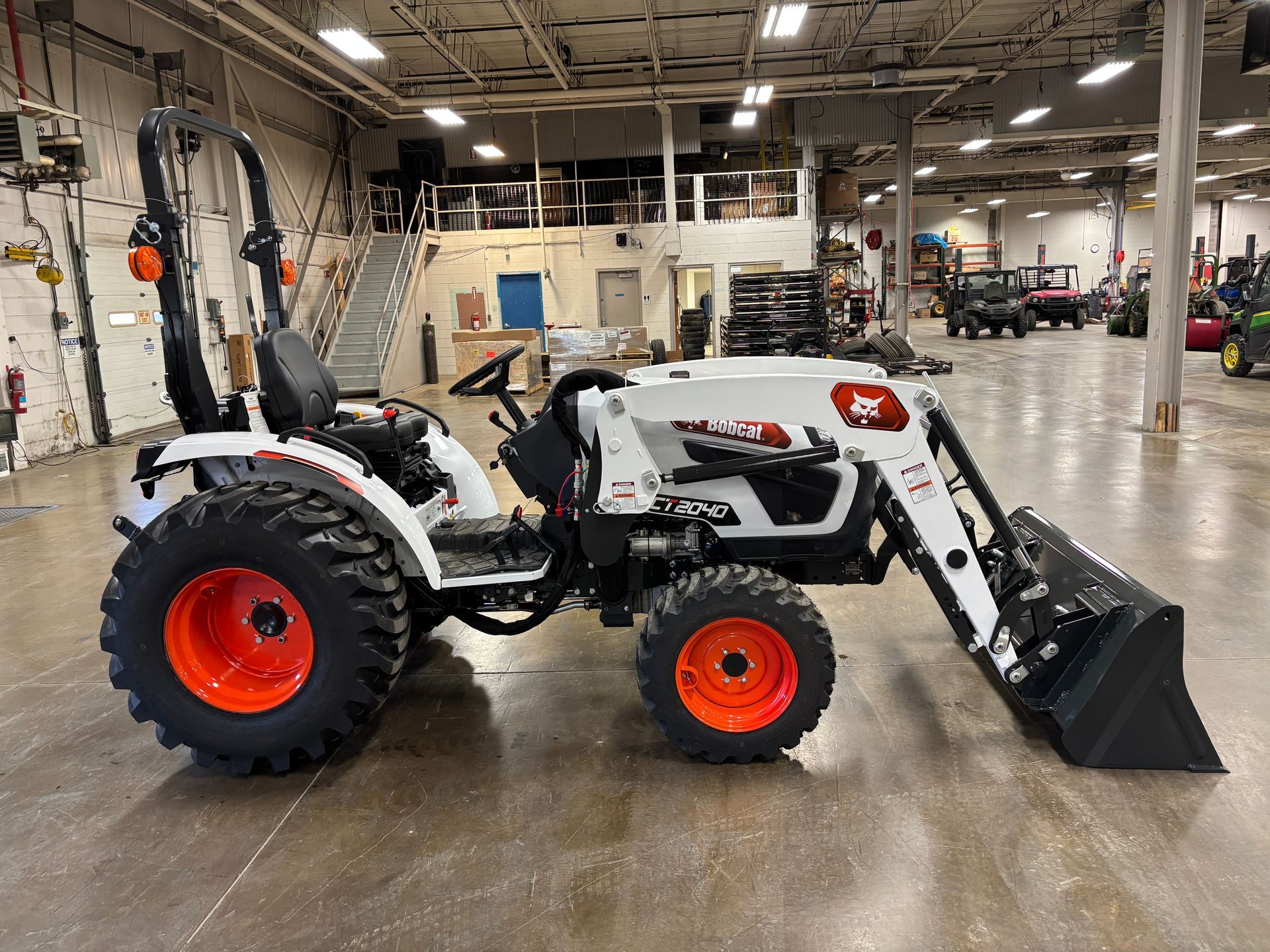 White Bobcat tractor with orange wheels and front loader, parked inside a large warehouse.